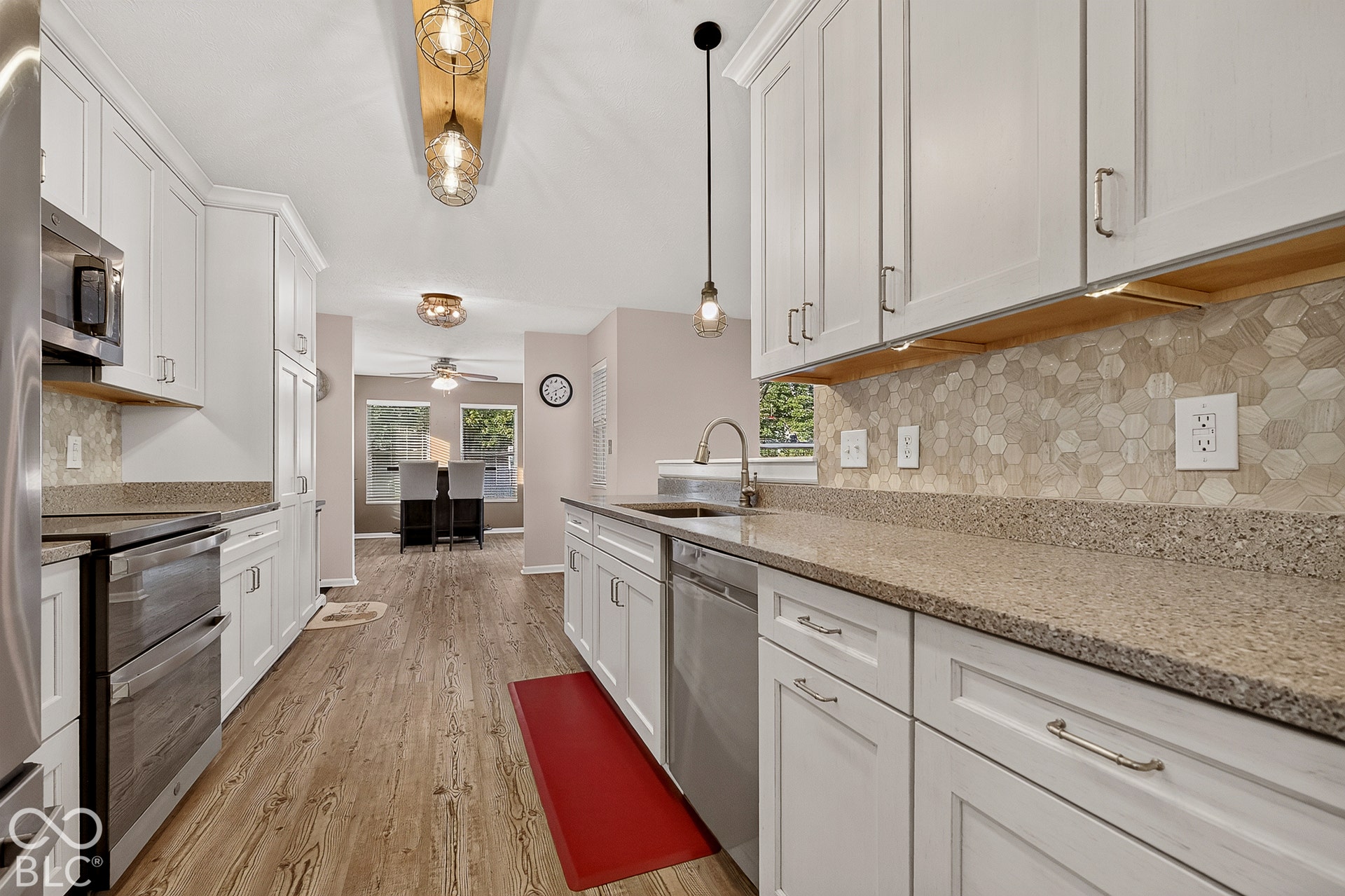 White cabinetry, stainless steel appliances, wood-finish flooring, stone countertops, and a hexagonal tile backsplash