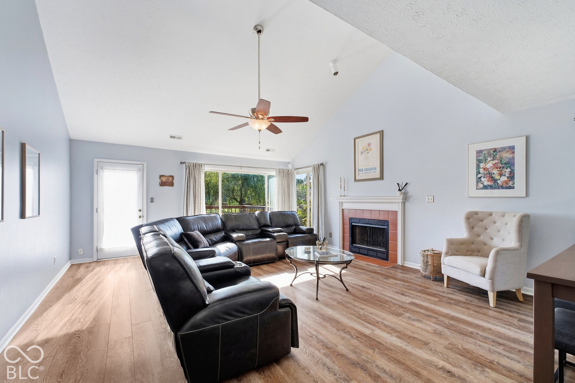 Vaulted ceiling with ceiling fan, wood-finish flooring, fireplace with white mantle, and sliding glass door