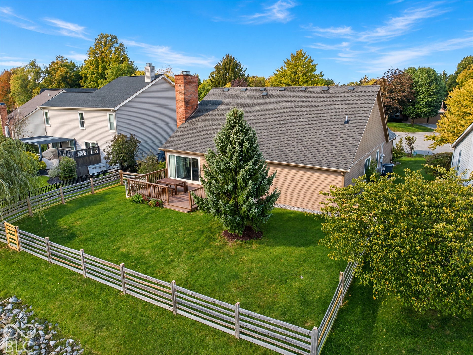 Expansive green lawn with a wood plank fence, mature trees, and a wood deck