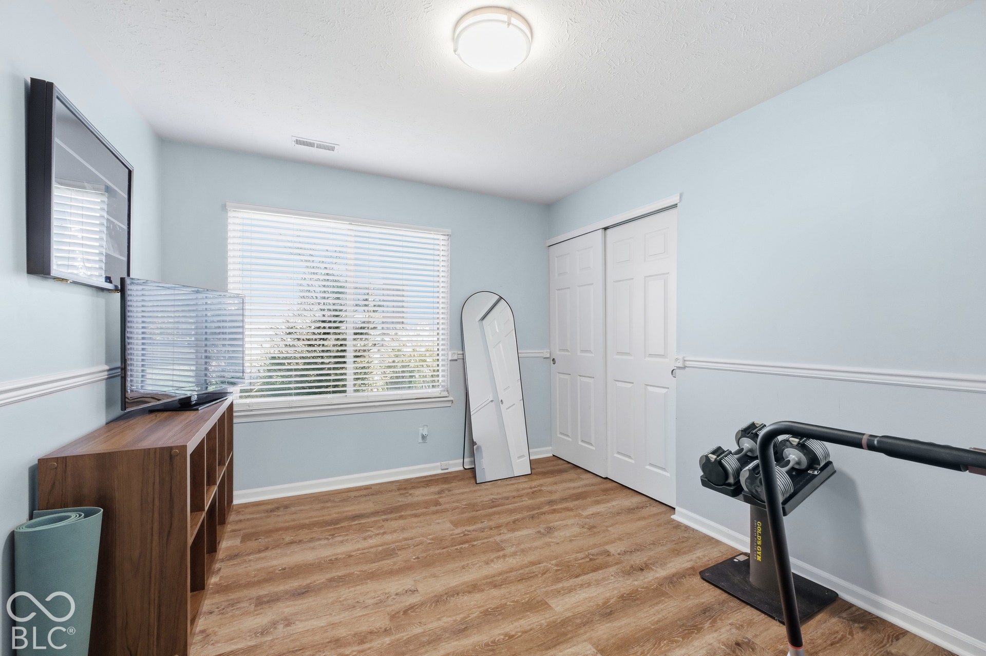 Wood-finish flooring, single window with blinds, bi-fold closet doors, and crown molding