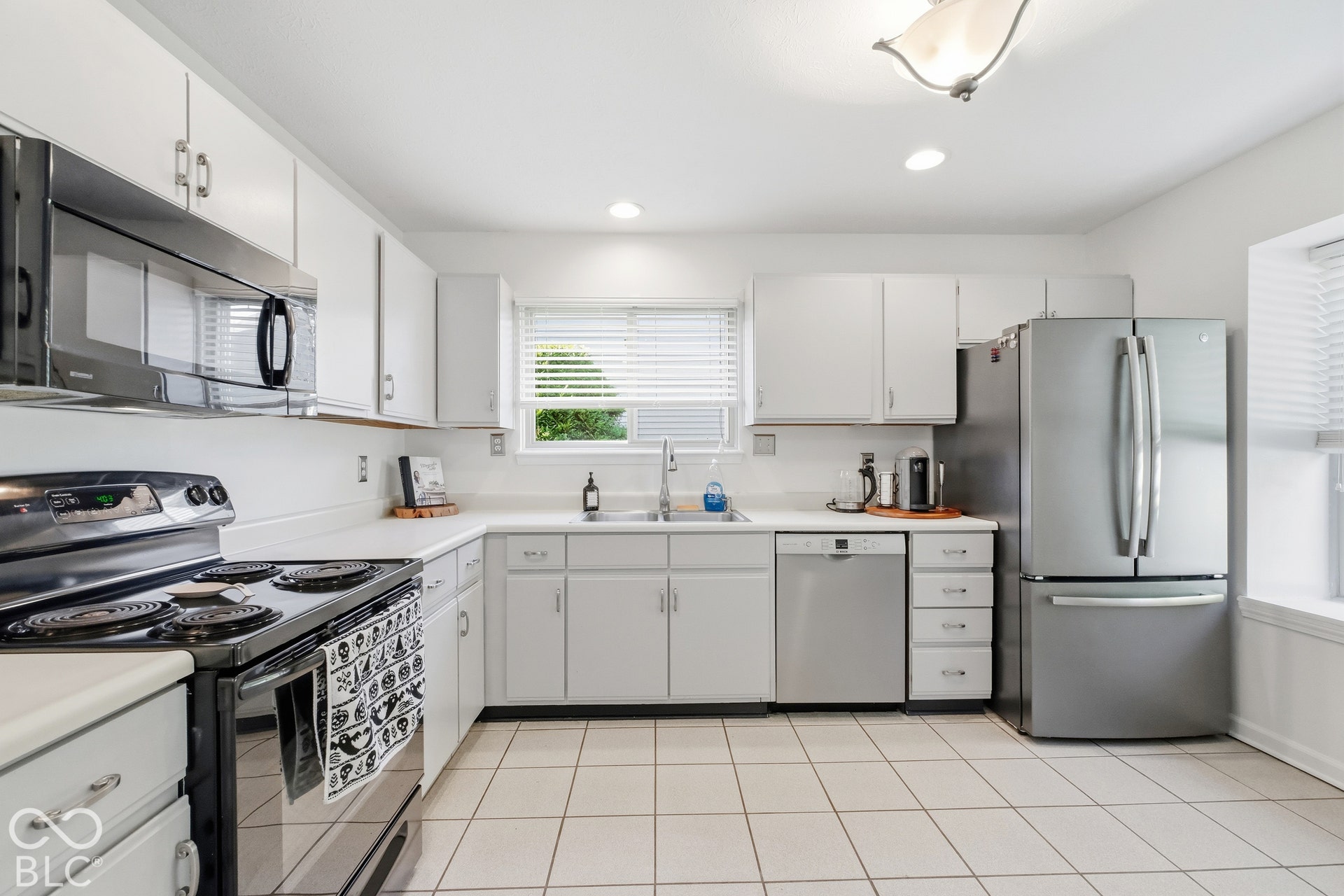 White cabinetry with brushed nickel hardware, stainless steel appliances, tile flooring, and a window above the sink
