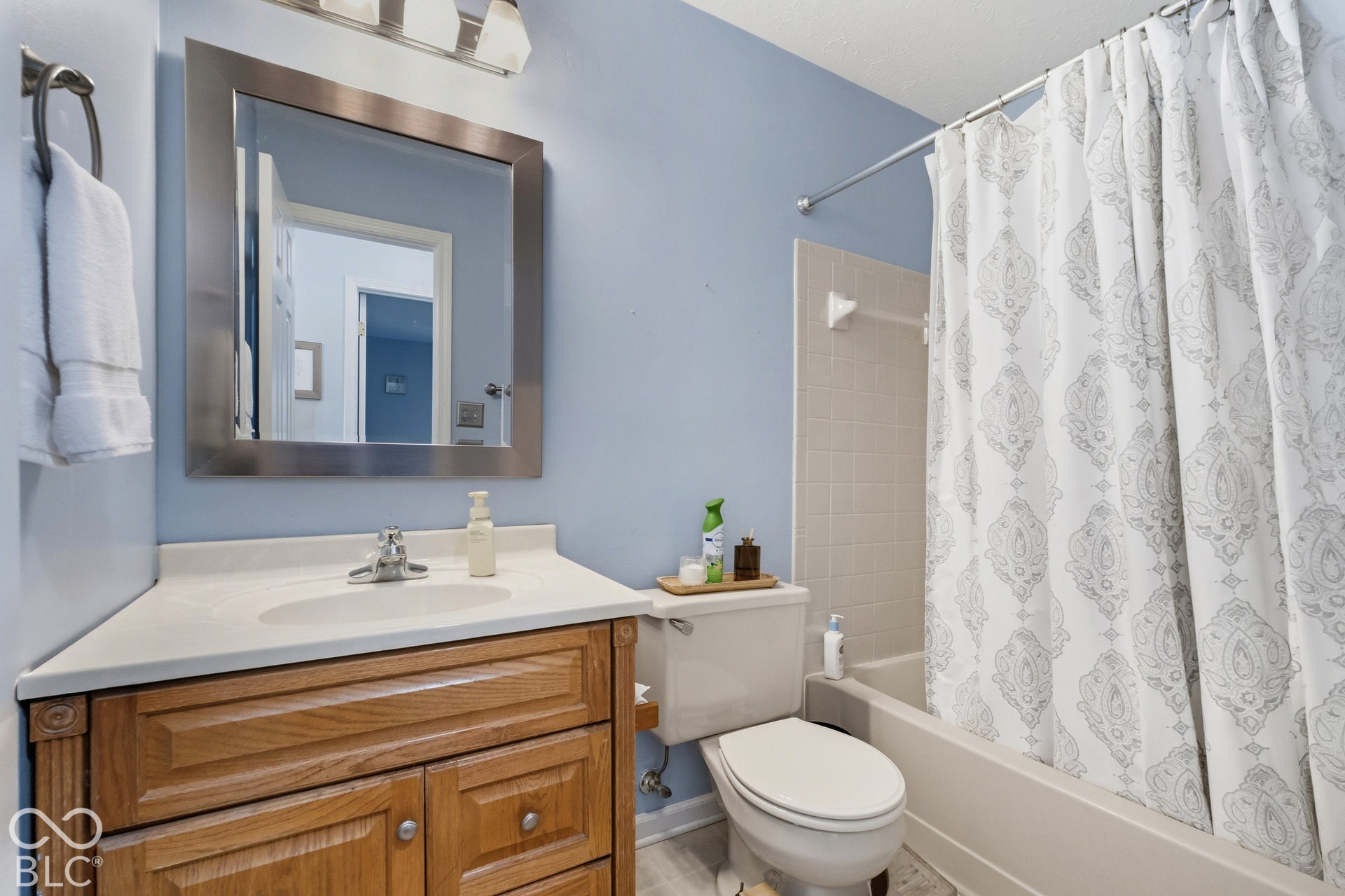Bathroom featuring a wood-finish vanity with a single sink, a framed mirror, and a tub with a shower