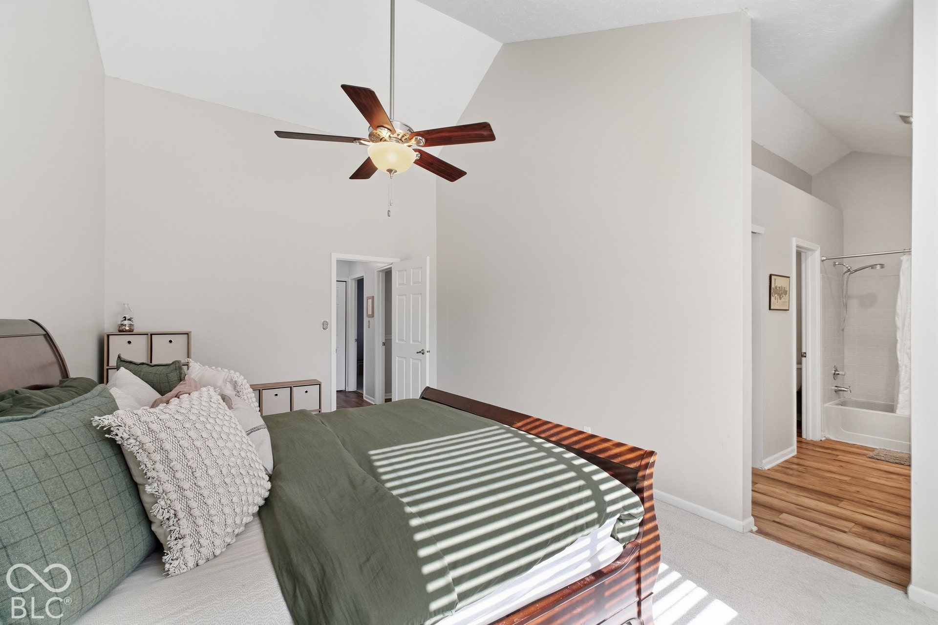 Vaulted ceilings, a ceiling fan with light fixture, carpeted flooring, and an adjoining bathroom with a tub and shower combination