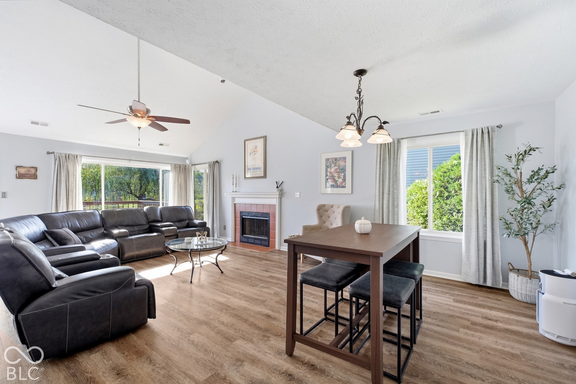 Vaulted ceiling with a ceiling fan, wood-finish flooring, fireplace with a tile surround and mantel, and large sliding glass doors leading to an outdoor deck
