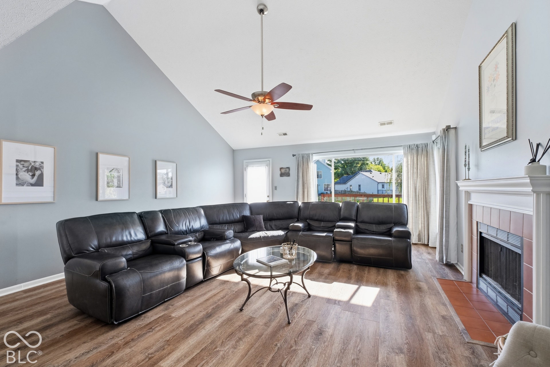 Vaulted ceiling, wood-finish flooring, fireplace with tile surround, ceiling fan, and sliding glass door