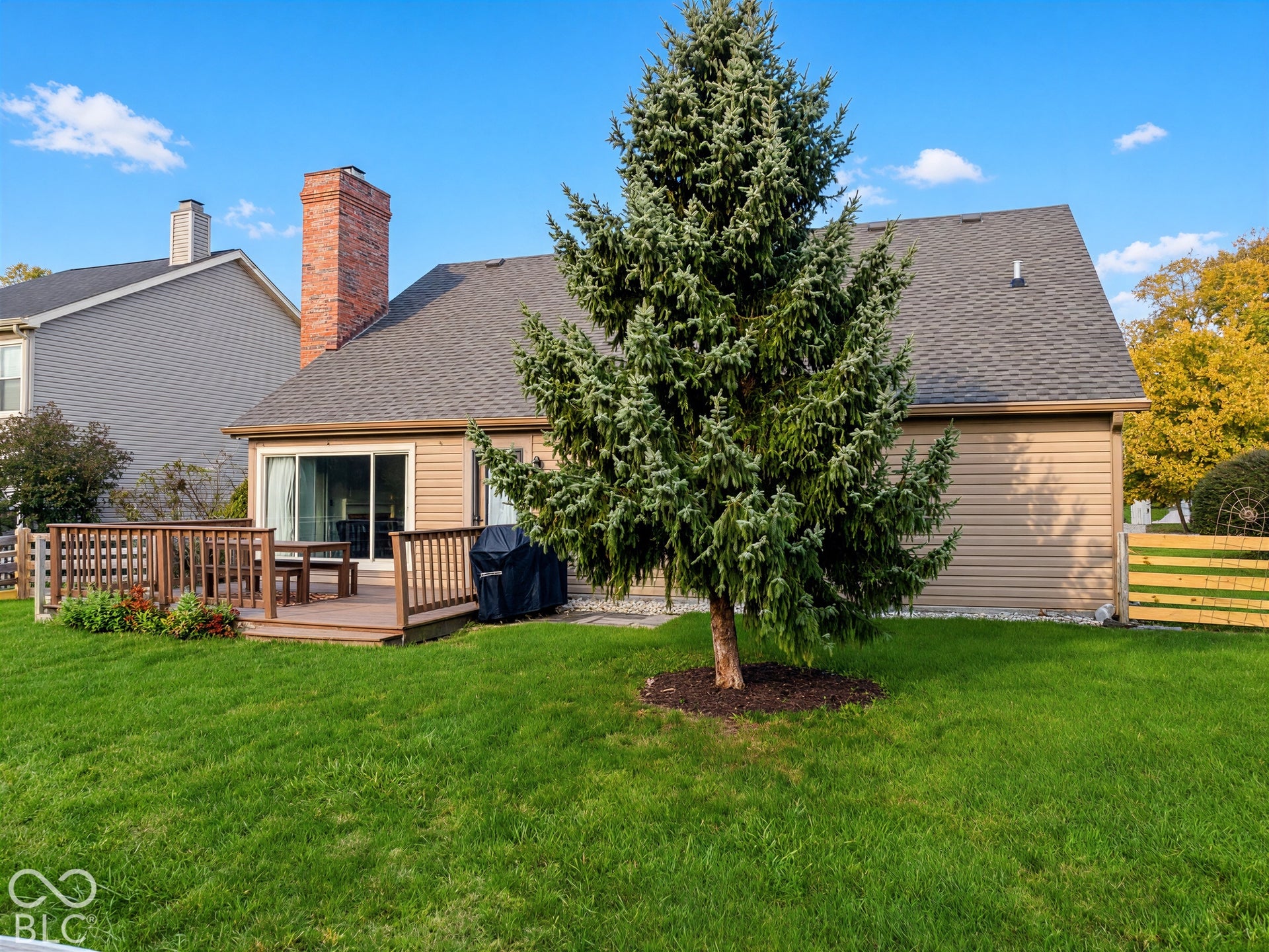 Expansive green lawn, wood-finish deck with railing, sliding glass door, brick chimney, and siding exterior