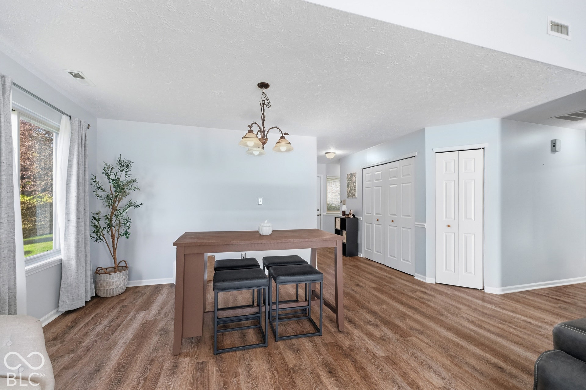 Wood-finish flooring throughout, bay window with white trim, and a bronze-finish chandelier