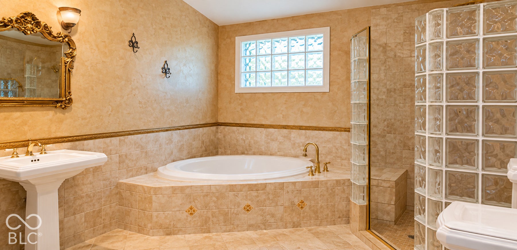 Pedestal sink with brass-finish faucet, tiled soaking tub, glass block shower enclosure, and glass block window