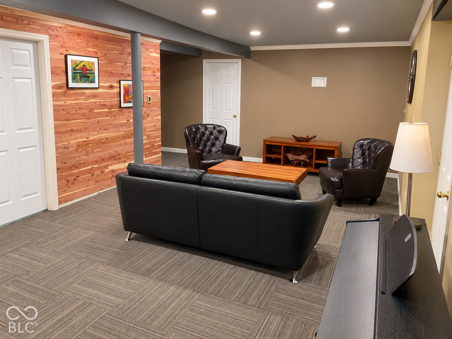 Recessed lighting illuminates a space featuring a wood-paneled accent wall, neutral-toned walls, and patterned carpet flooring
