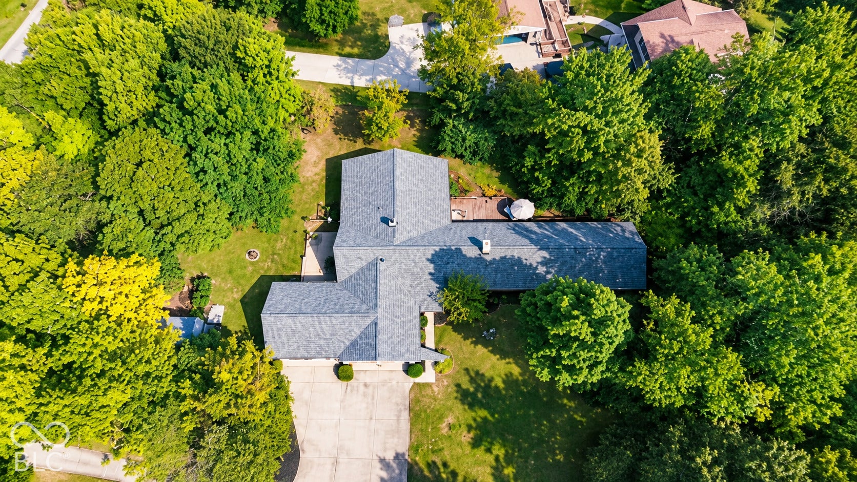 Expansive property featuring mature trees, blacktop driveway, and a large roofline