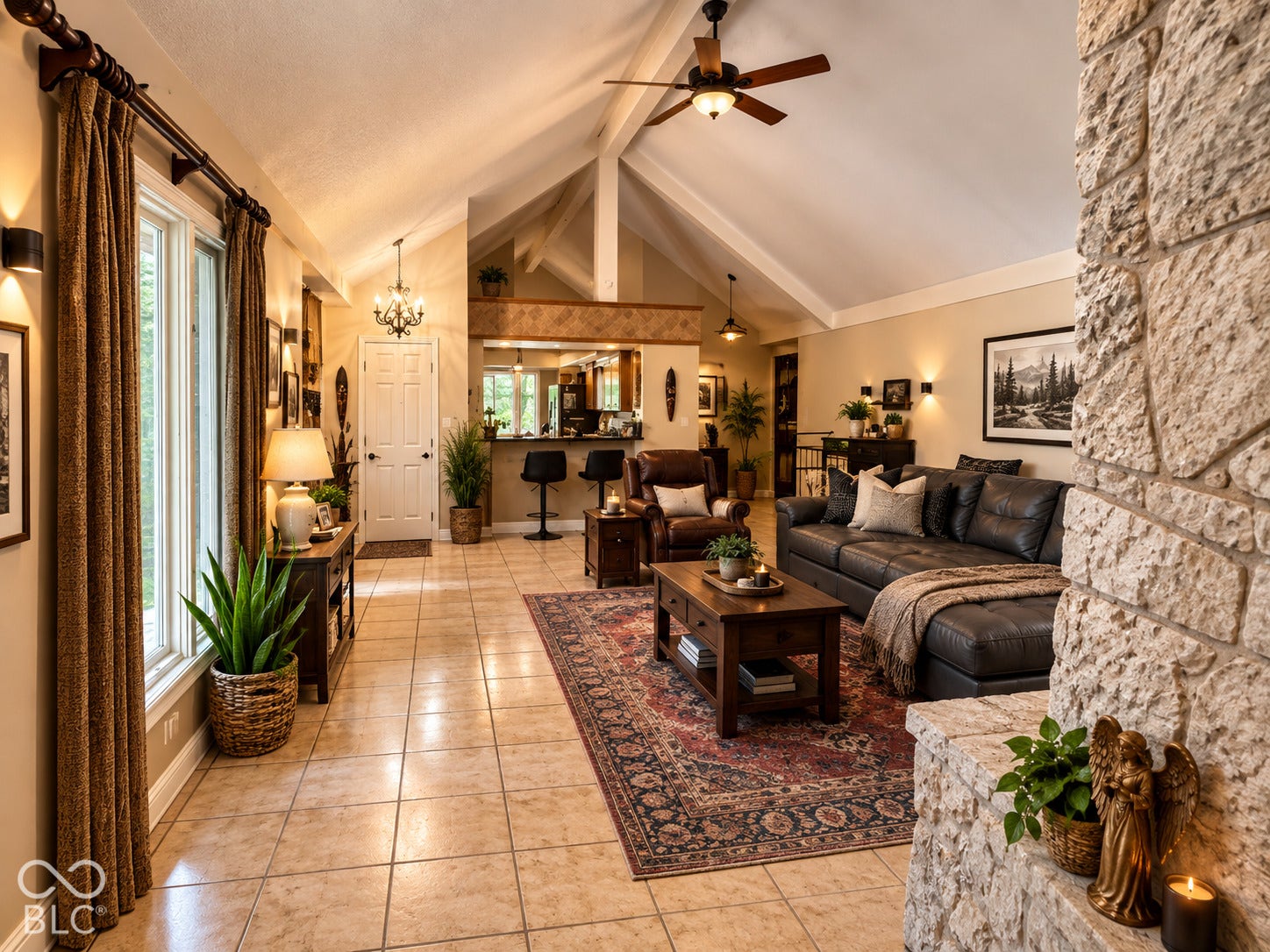 Vaulted ceiling with exposed beams, stone-clad fireplace, tile flooring, recessed bar area, and ceiling fan with integrated lighting