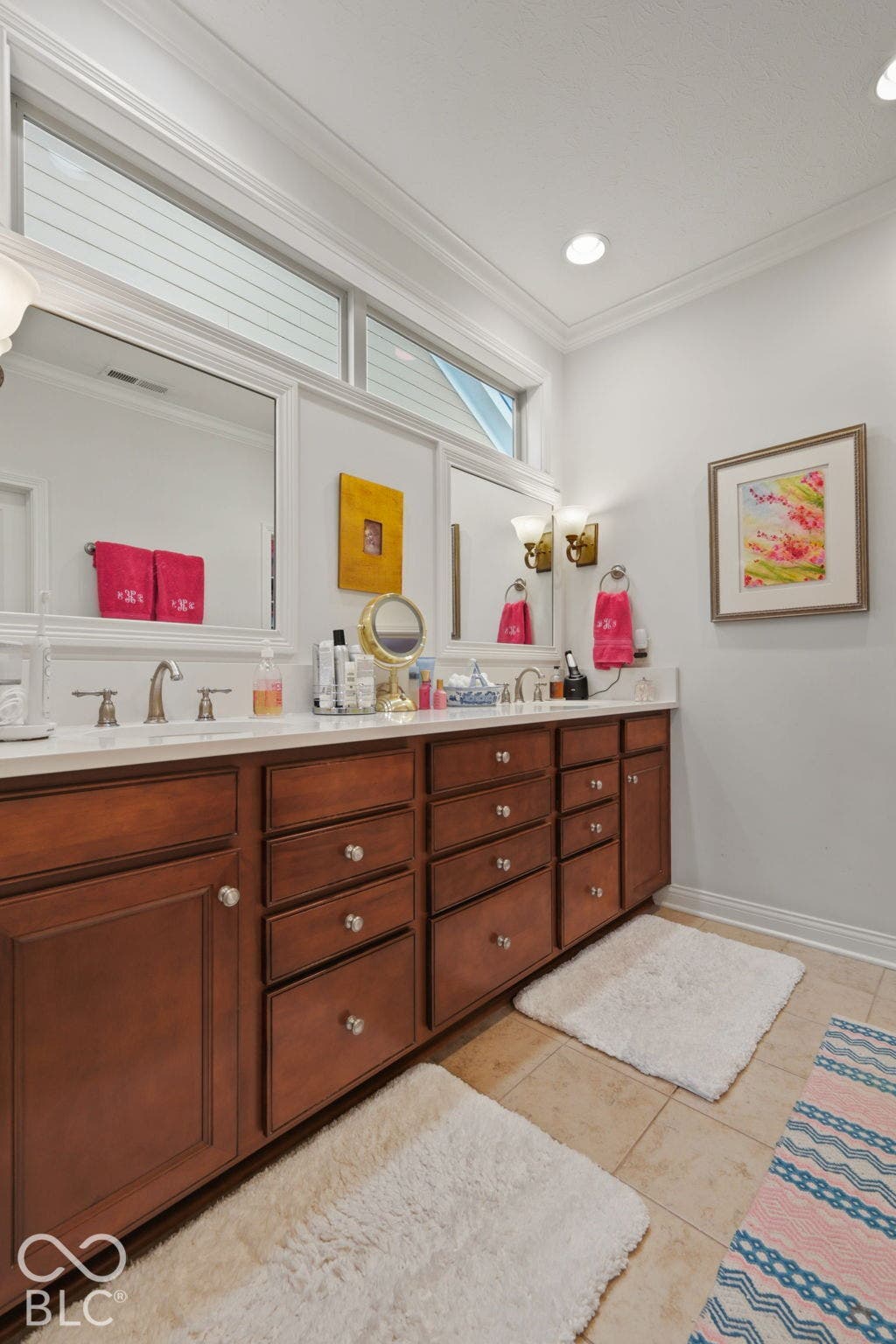 Dual vanity with integrated sinks, rich wood cabinetry, polished chrome fixtures, and white countertops