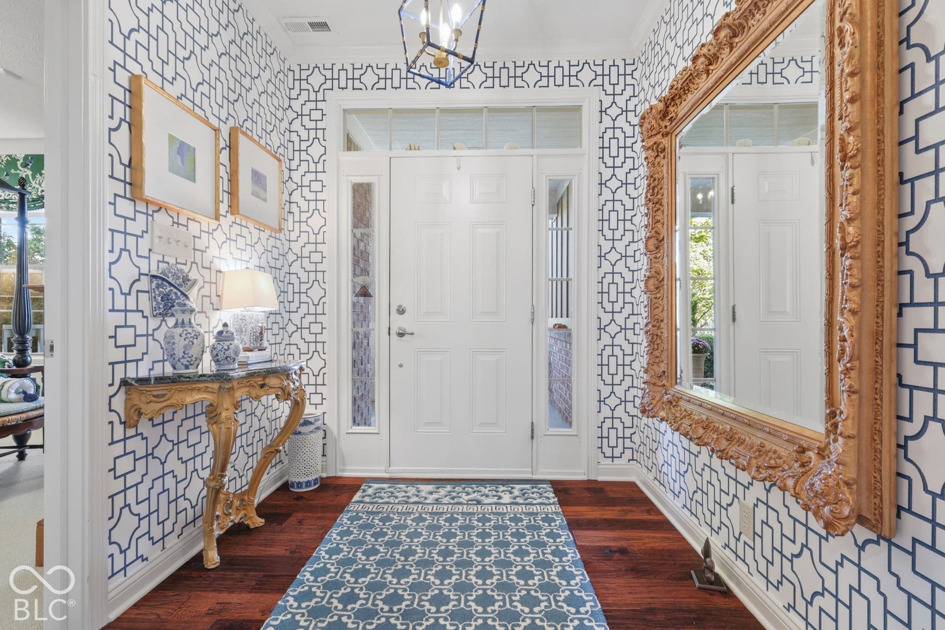 Hardwood flooring, decorative patterned wallpaper, and a transom window above the front entry