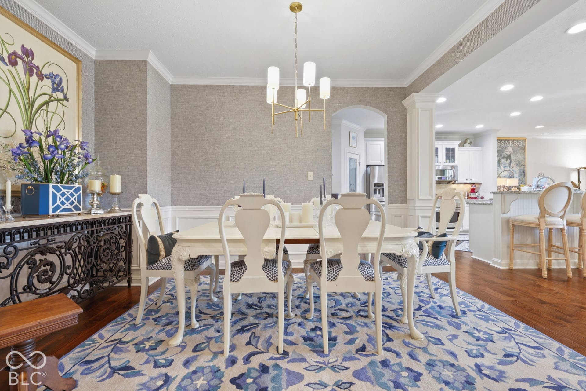 Hardwood flooring, crown molding, wainscoting, arched doorway, and a modern chandelier