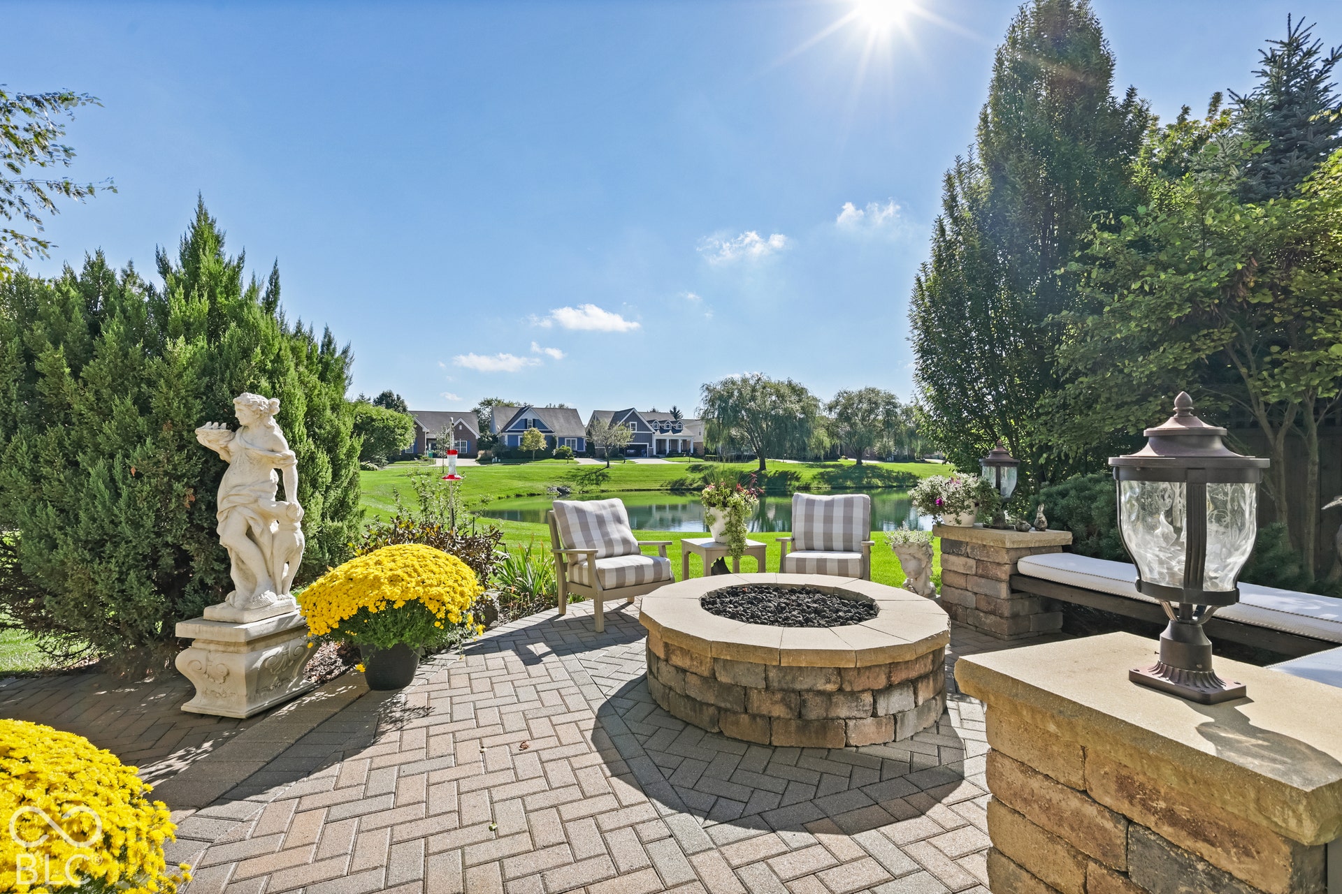 Virtually Altered - Paver patio featuring a built-in fire pit, stone-clad seating, and mature landscaping
