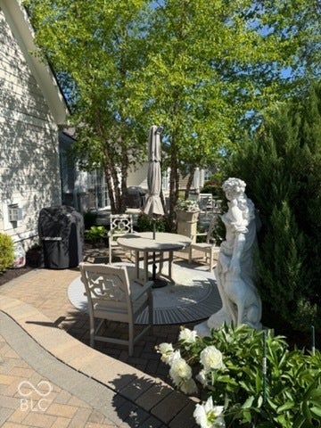 Paver patio with a circular inlay, surrounded by mature trees and shrubs