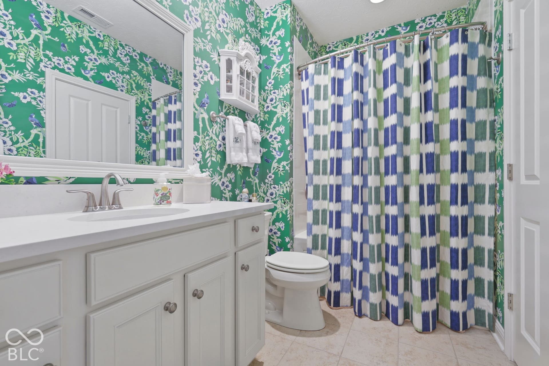 Vanity with white cabinetry and integrated sink, brushed nickel faucet, large wall mirror with decorative frame, and tiled flooring