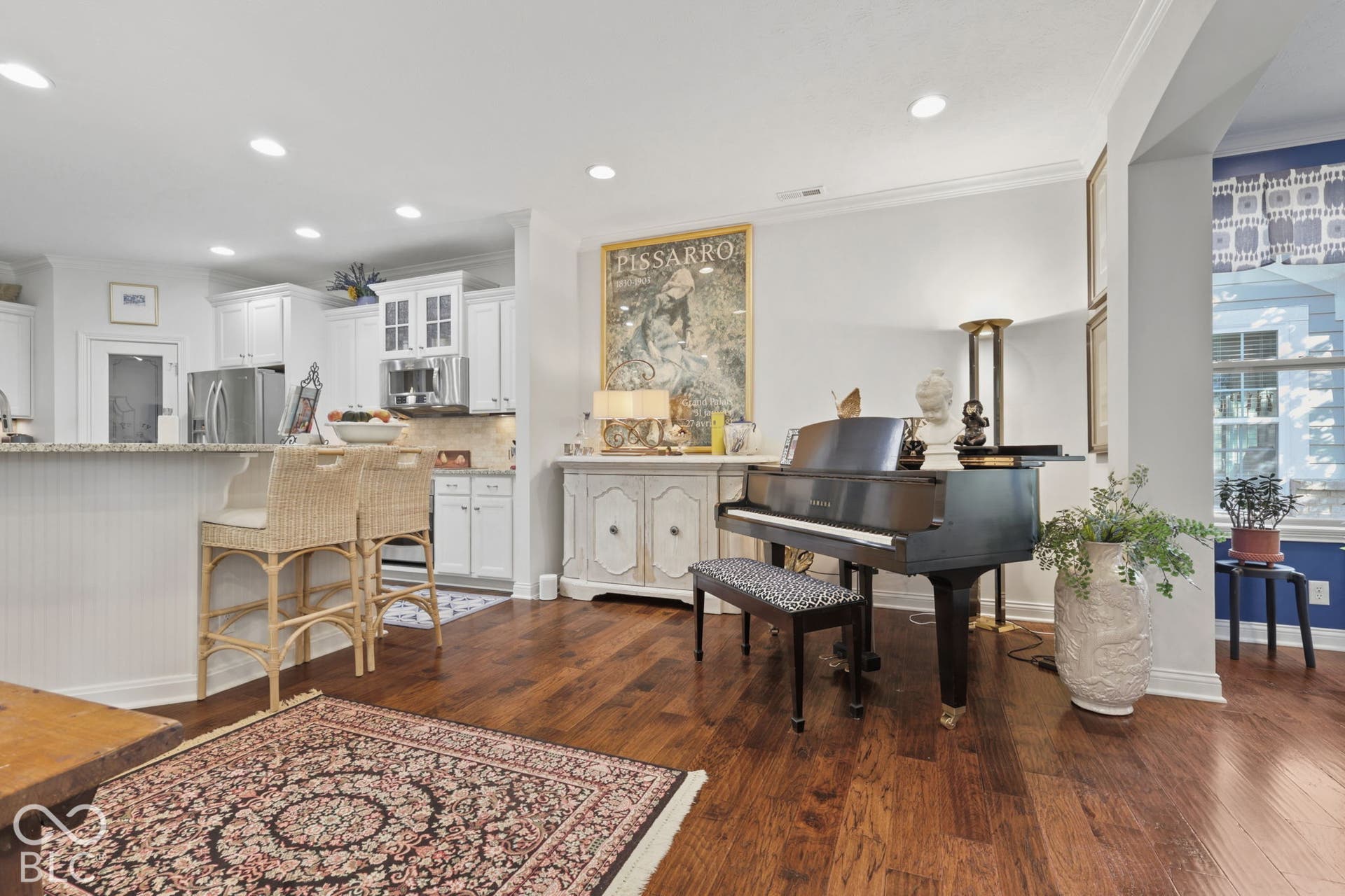 Wood-finish flooring throughout, recessed lighting, white kitchen cabinetry, stainless steel appliances, and a kitchen island with seating