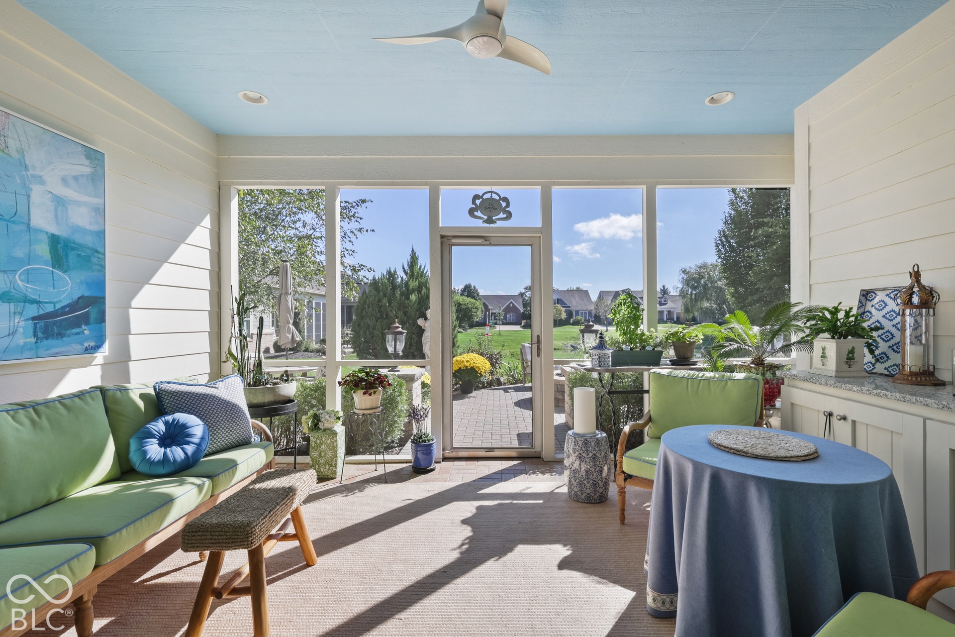 Virtually Altered - Screened porch featuring a light blue ceiling, ceiling fan, white shiplap walls, built-in cabinetry with a light-colored countertop, and a glass-paneled entry door