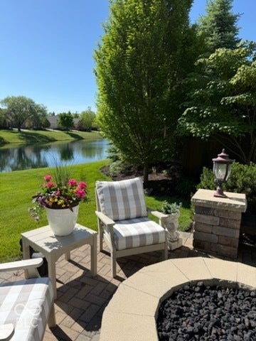 Paver patio with a built-in fire pit, stone-clad pillar, and mature perimeter landscaping