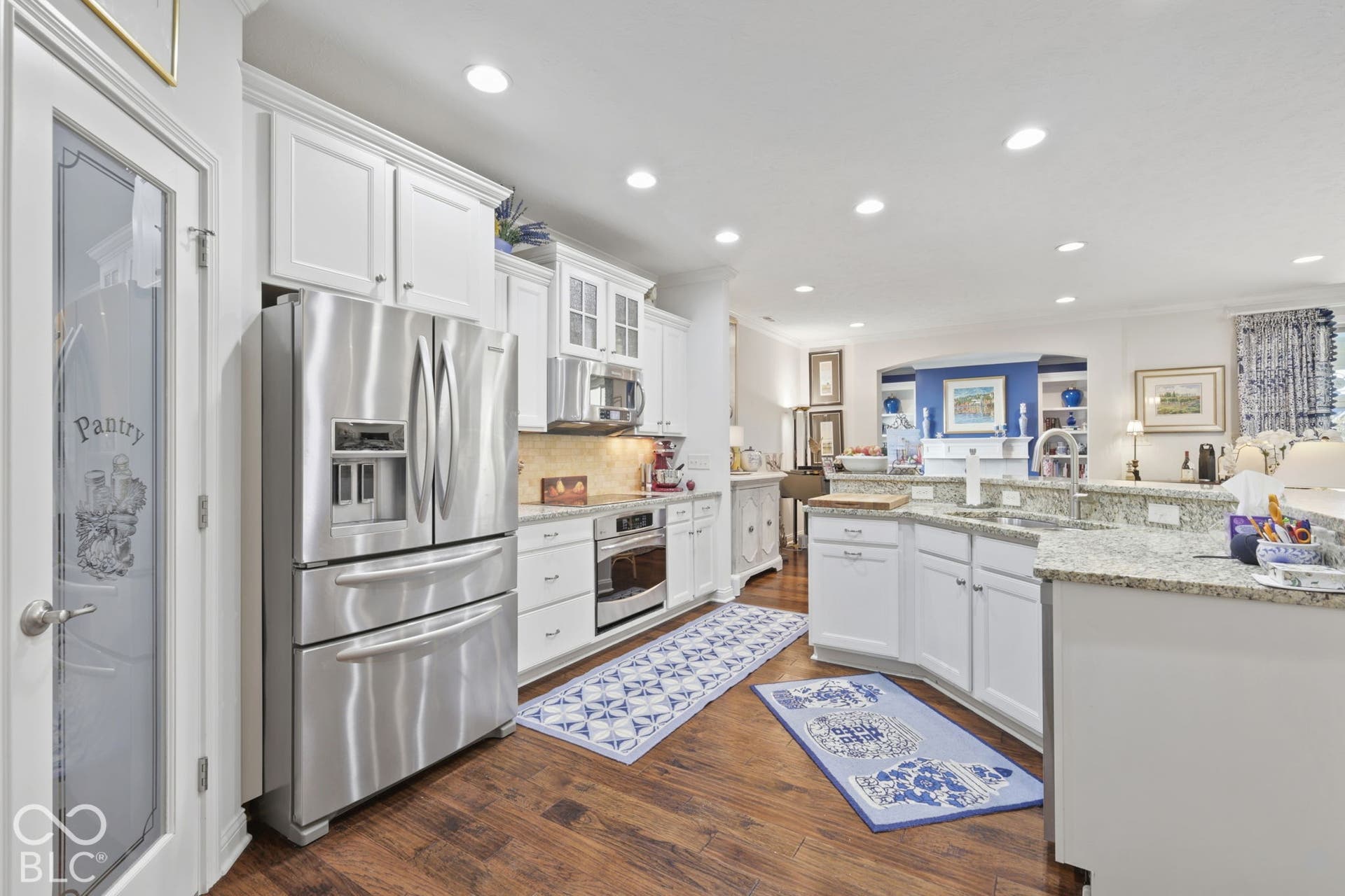 Gourmet kitchen featuring stainless steel appliances, granite countertops, white cabinetry, wood-finish flooring, and recessed lighting