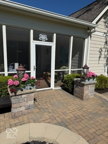 Screened porch with clear panels, exterior siding, a shingled roof, paver patio, and stone fire pit surround