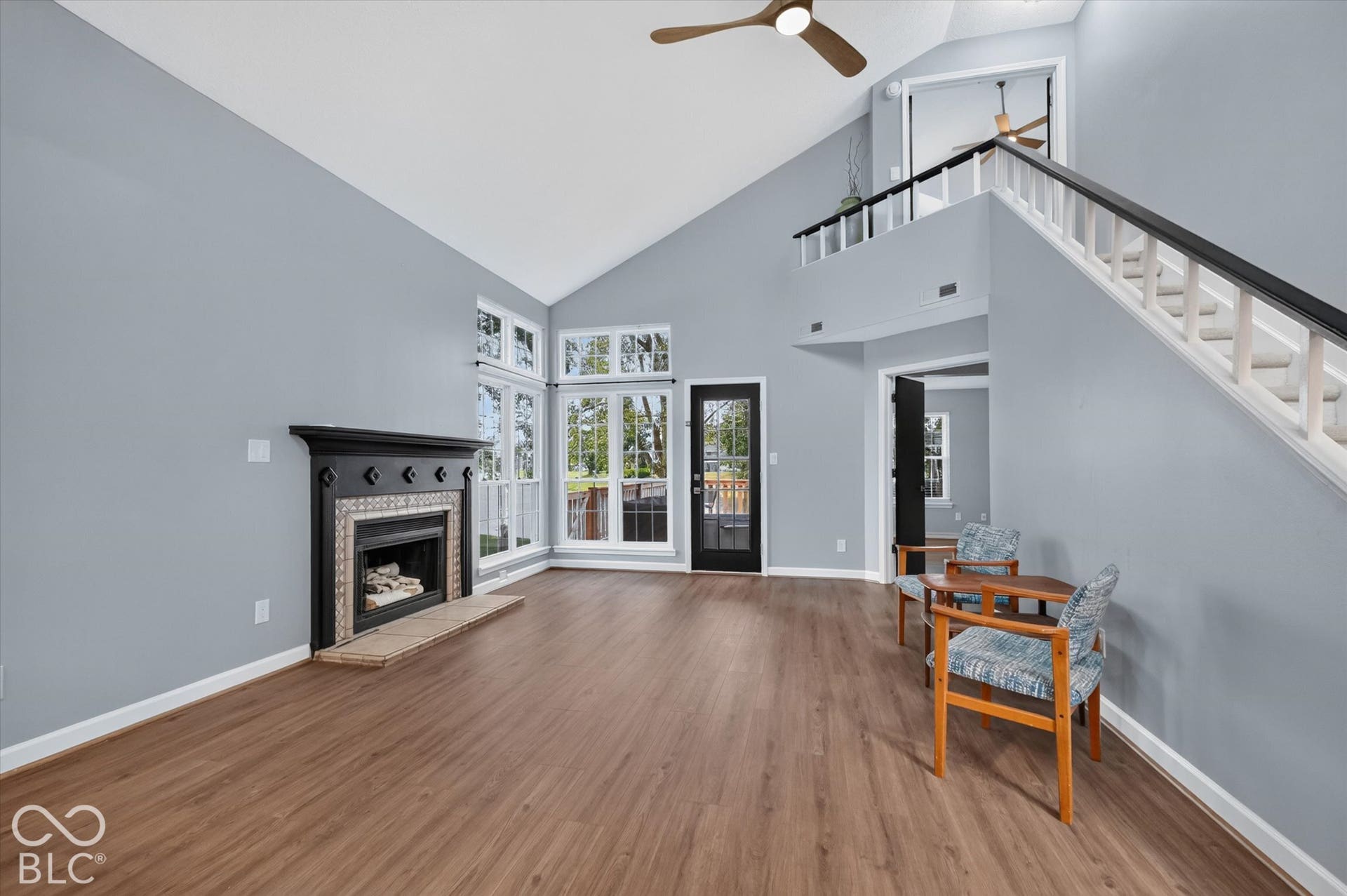 Vaulted ceiling with a ceiling fan, wood-finish flooring, and a fireplace with a decorative mantel
