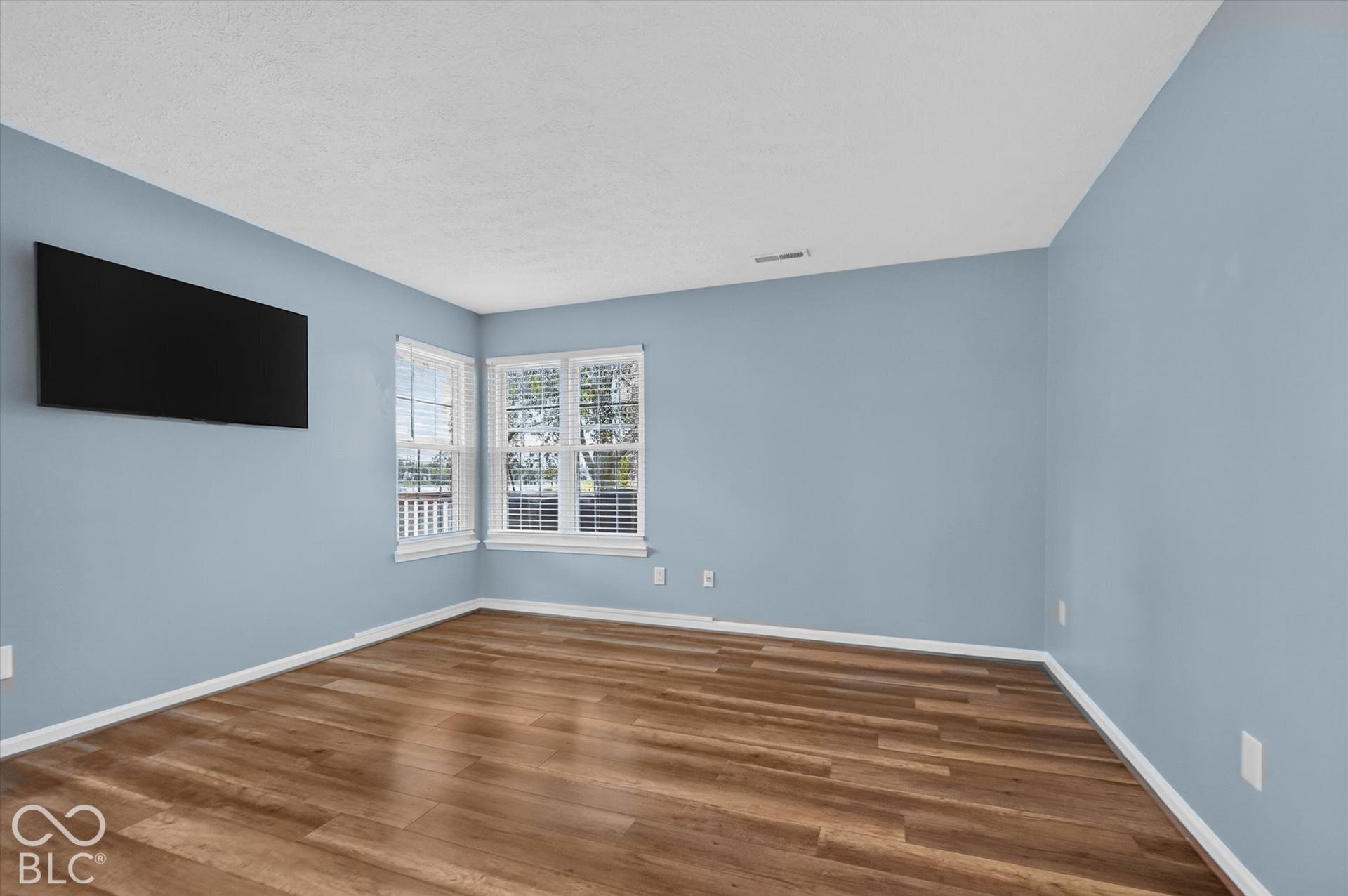 Wood-finish flooring with white trim, light blue painted walls, and window treatments