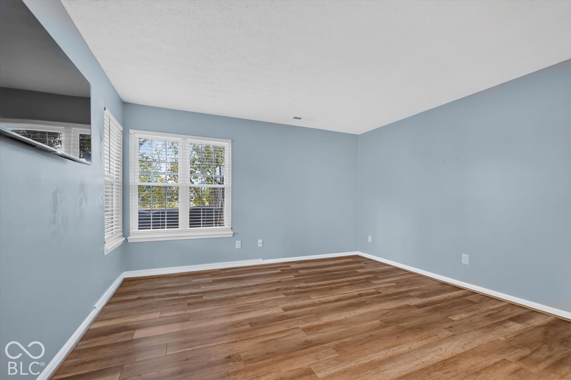 Wood-finish flooring, two windows with white blinds, and light blue walls