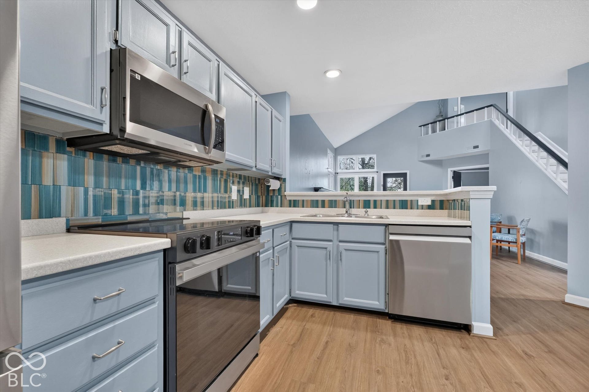 Kitchen featuring blue cabinetry, stainless steel appliances, a multi-tone tile backsplash, and light-toned countertops
