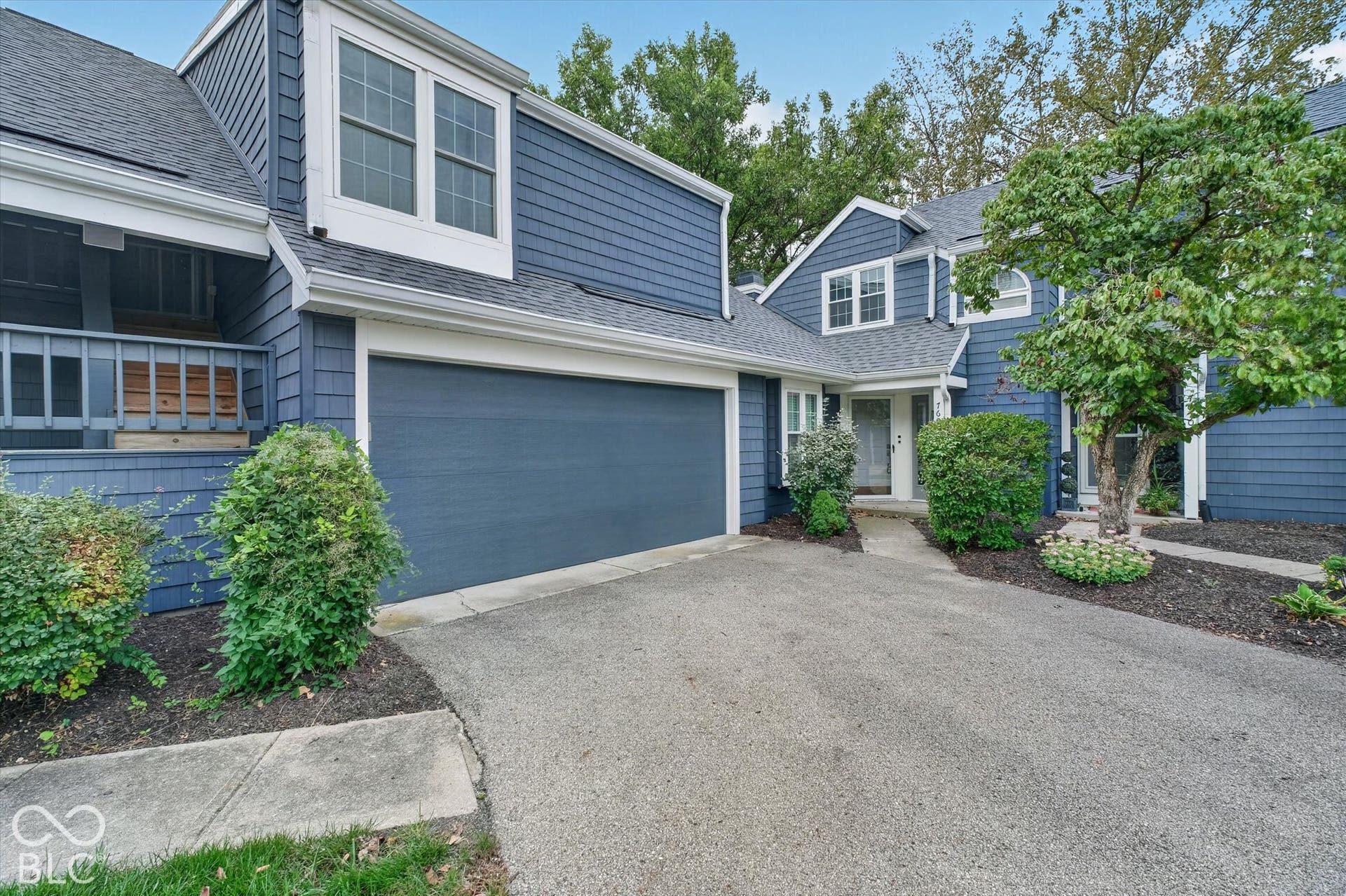 Blue shingle siding, an attached garage, white-framed windows, a covered front entry, and mature landscaping