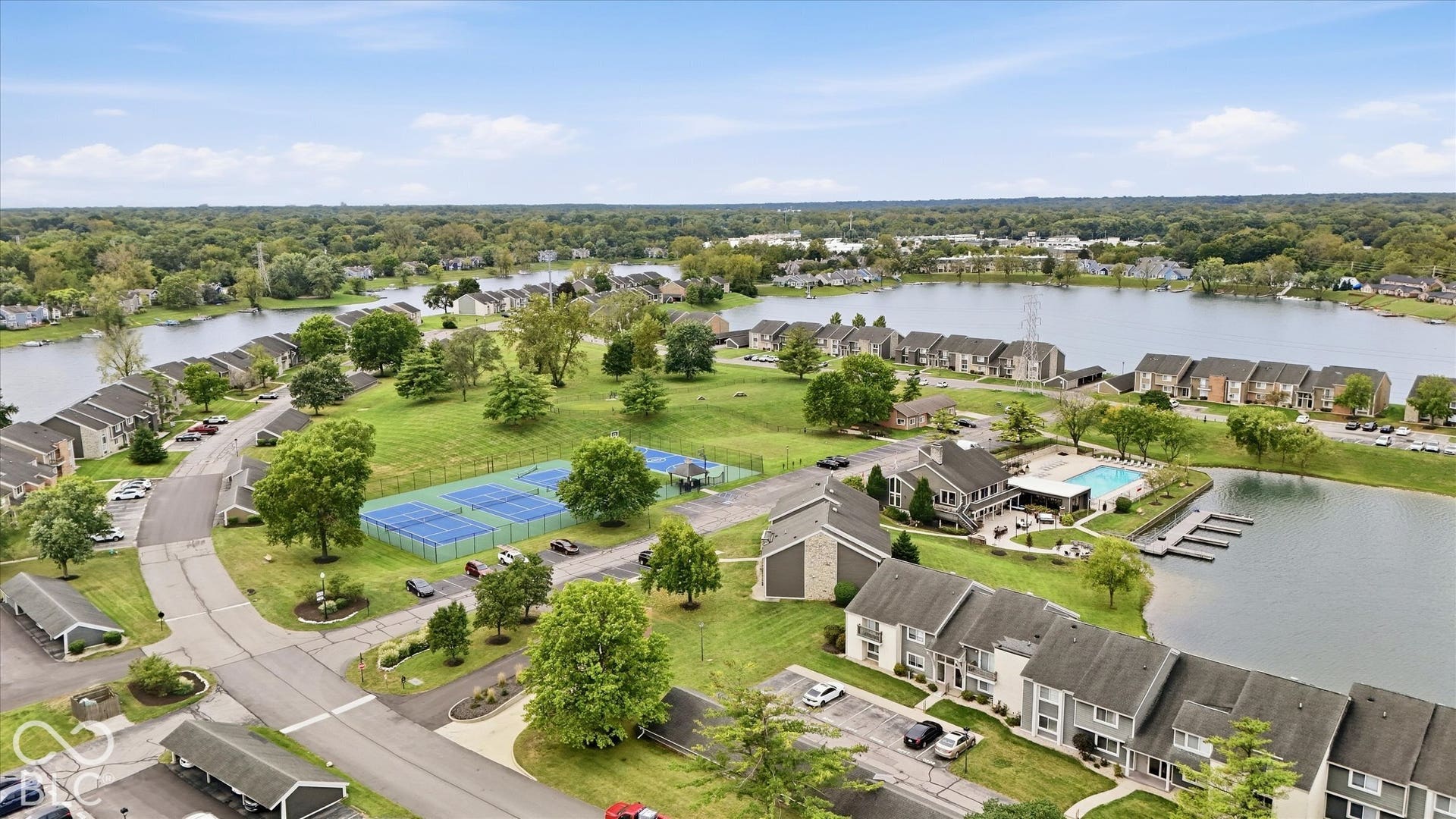 Expansive lakefront community featuring multiple residential buildings, a central lake, tennis courts, and a community pool with boat docks