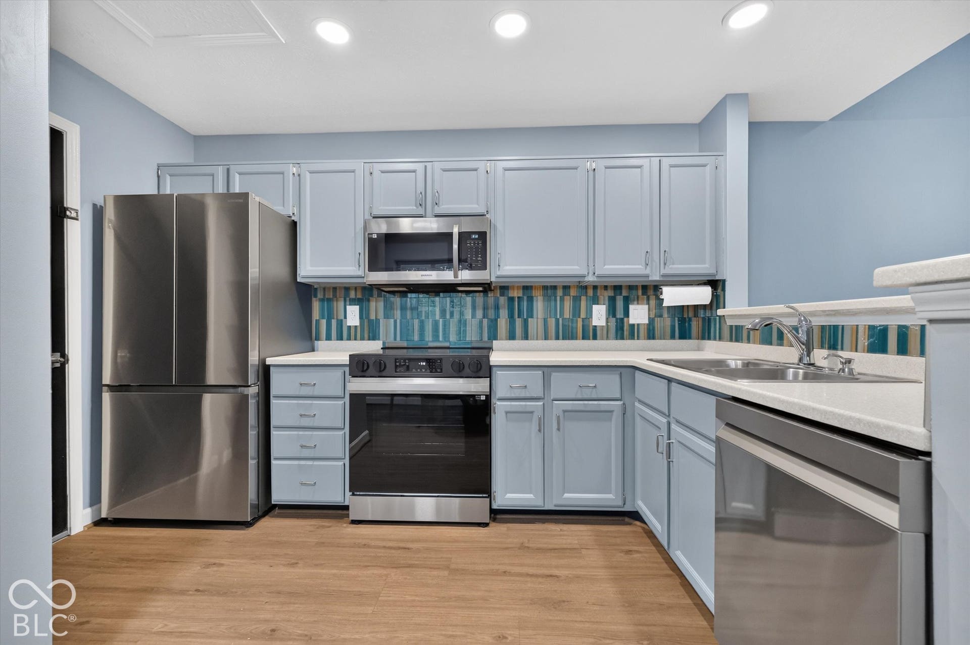 Kitchen featuring wood-finish flooring, light blue cabinetry, stainless steel appliances, light-colored countertops, and a tiled backsplash
