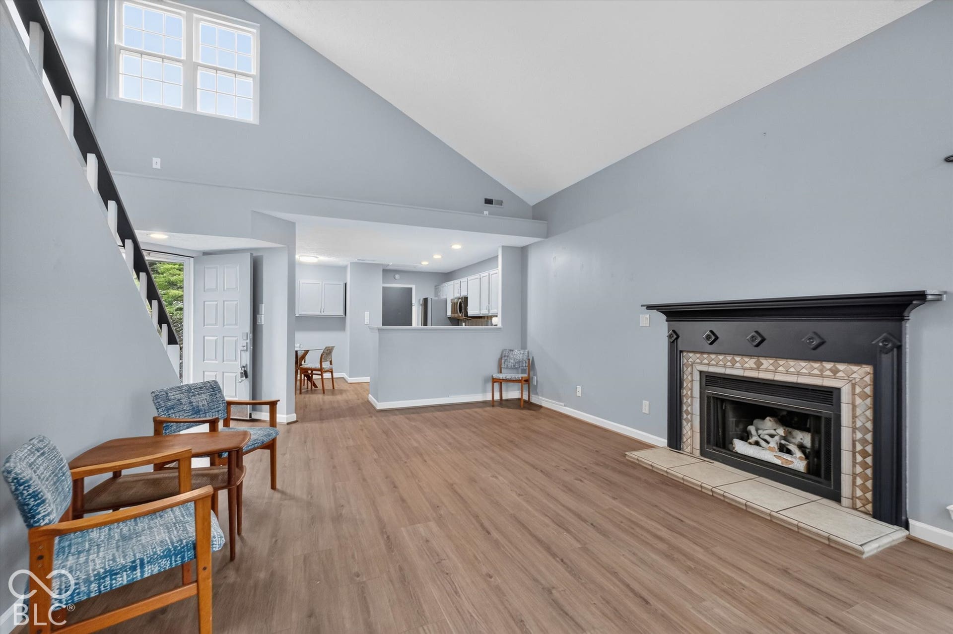 Vaulted ceiling with an upper transom window, wood-finish flooring, and a fireplace with a decorative tile surround and mantel