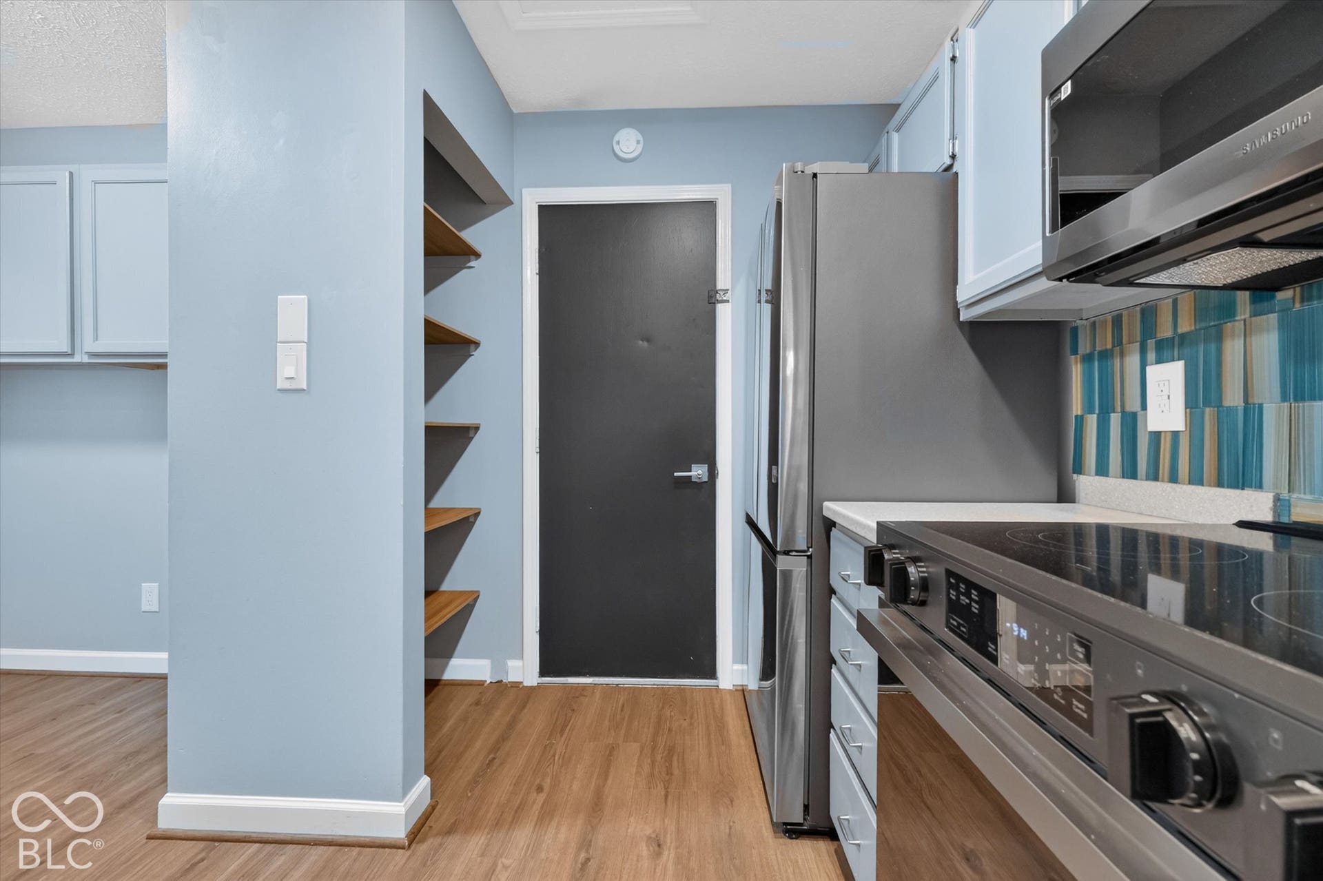 Wood-finish flooring, custom built-in shelving, stainless steel refrigerator, stainless steel range, and a tiled backsplash
