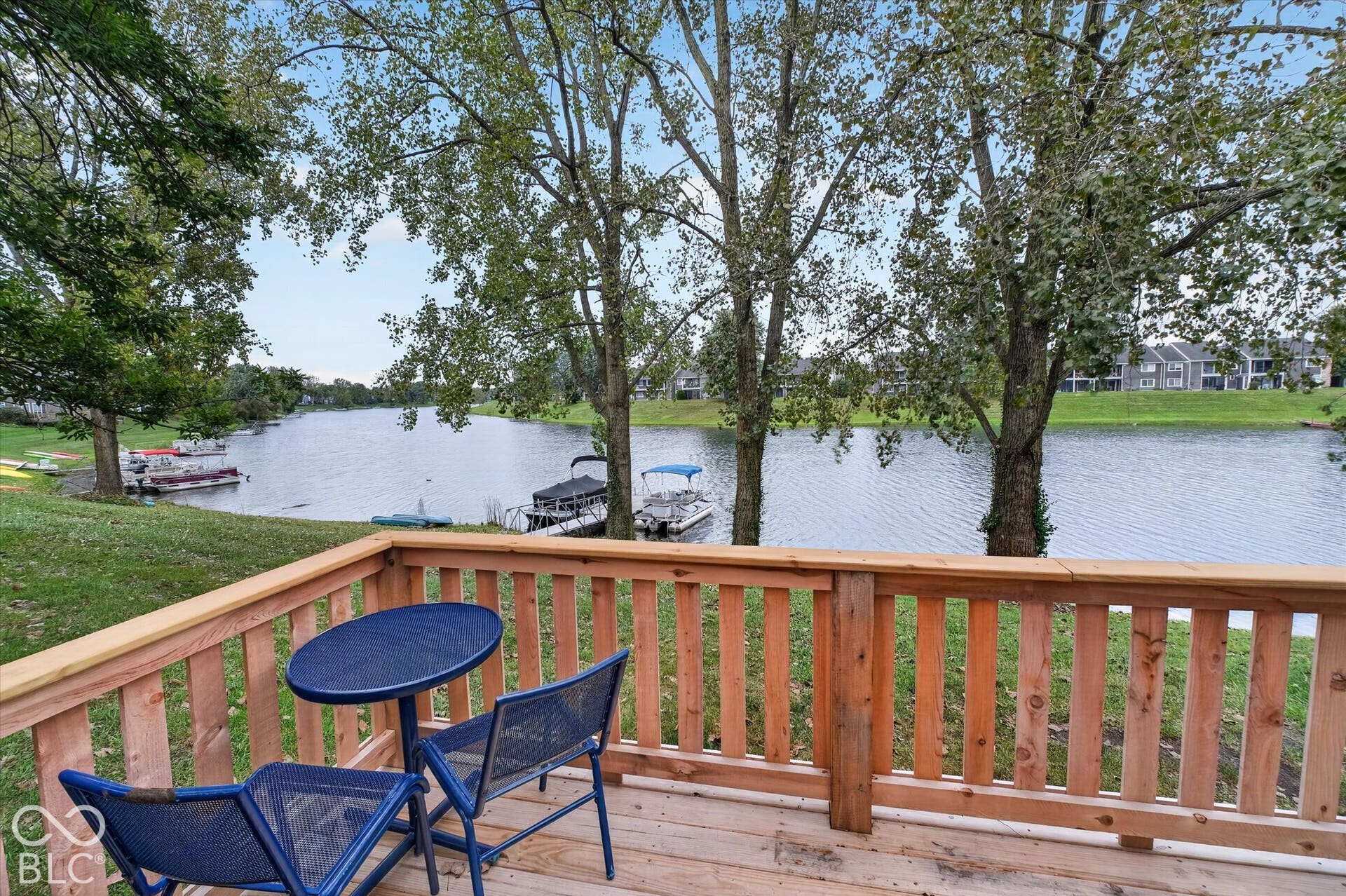 Waterfront property featuring a wood deck with a natural finish, wood railing, and mature trees along the shoreline