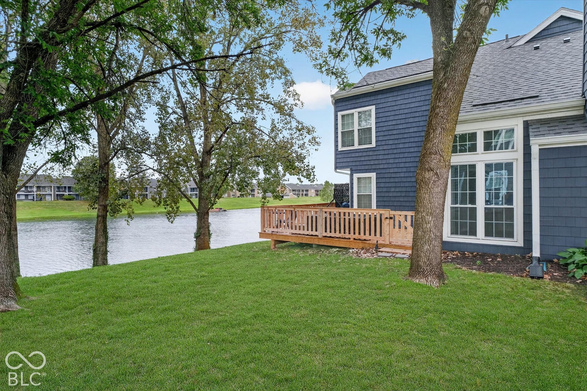 Expansive green lawn with mature trees, a wooden deck, and a body of water