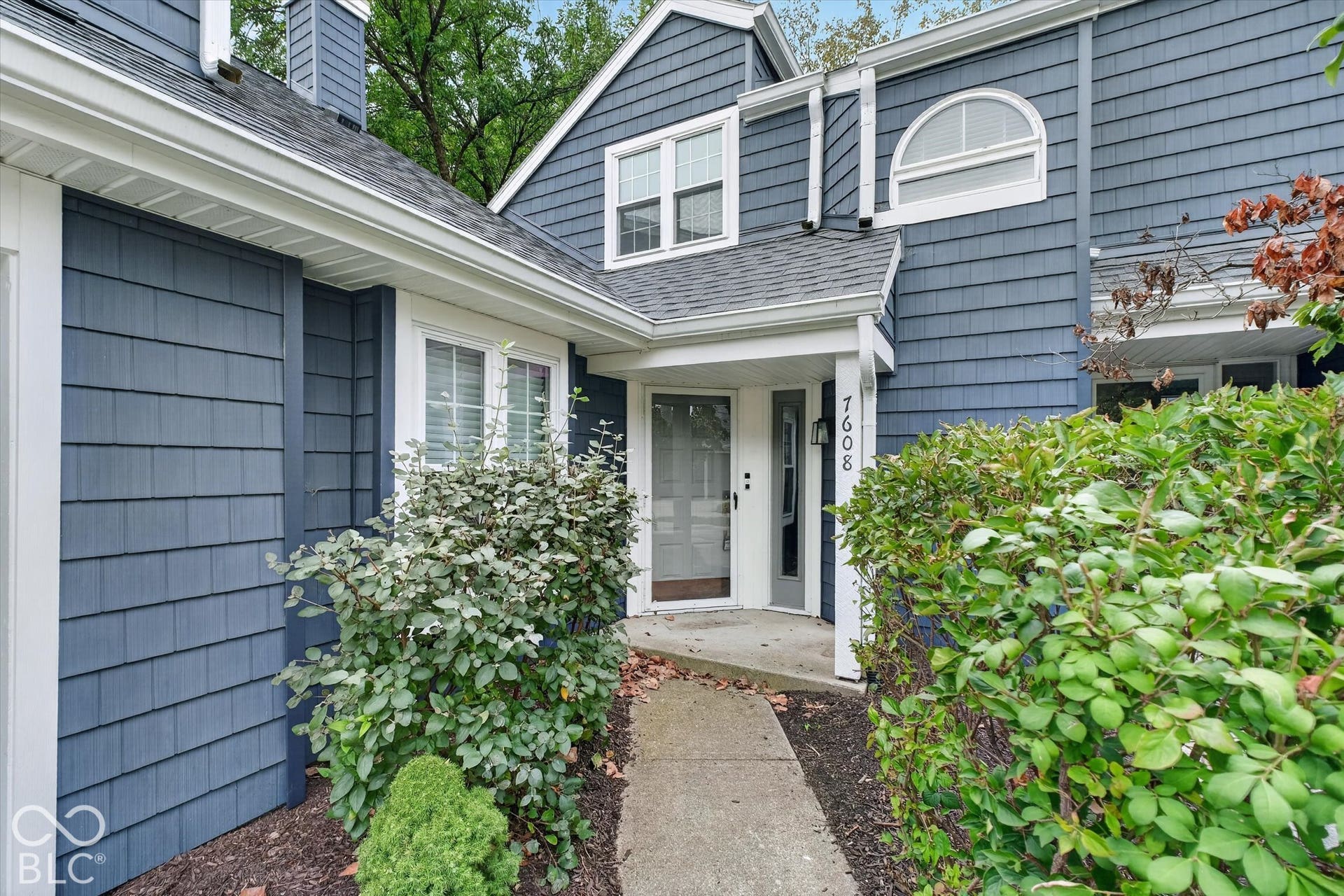 Blue shingle siding with white trim, a covered entry, and a concrete pathway