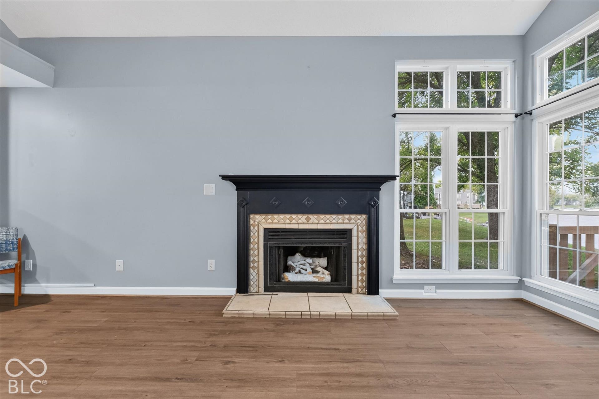 Wood-finish flooring, a black fireplace mantel, decorative fireplace surround, and multiple grid-style windows