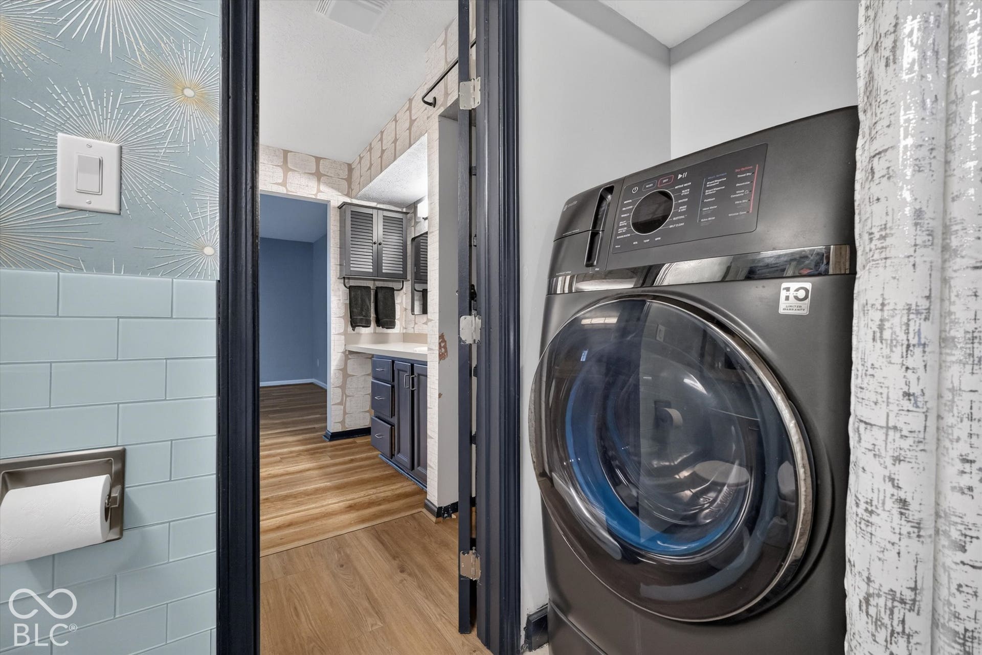 Front-load washing machine, blue subway tile wainscoting, wood-finish flooring, vanity with storage, wall-mounted cabinetry