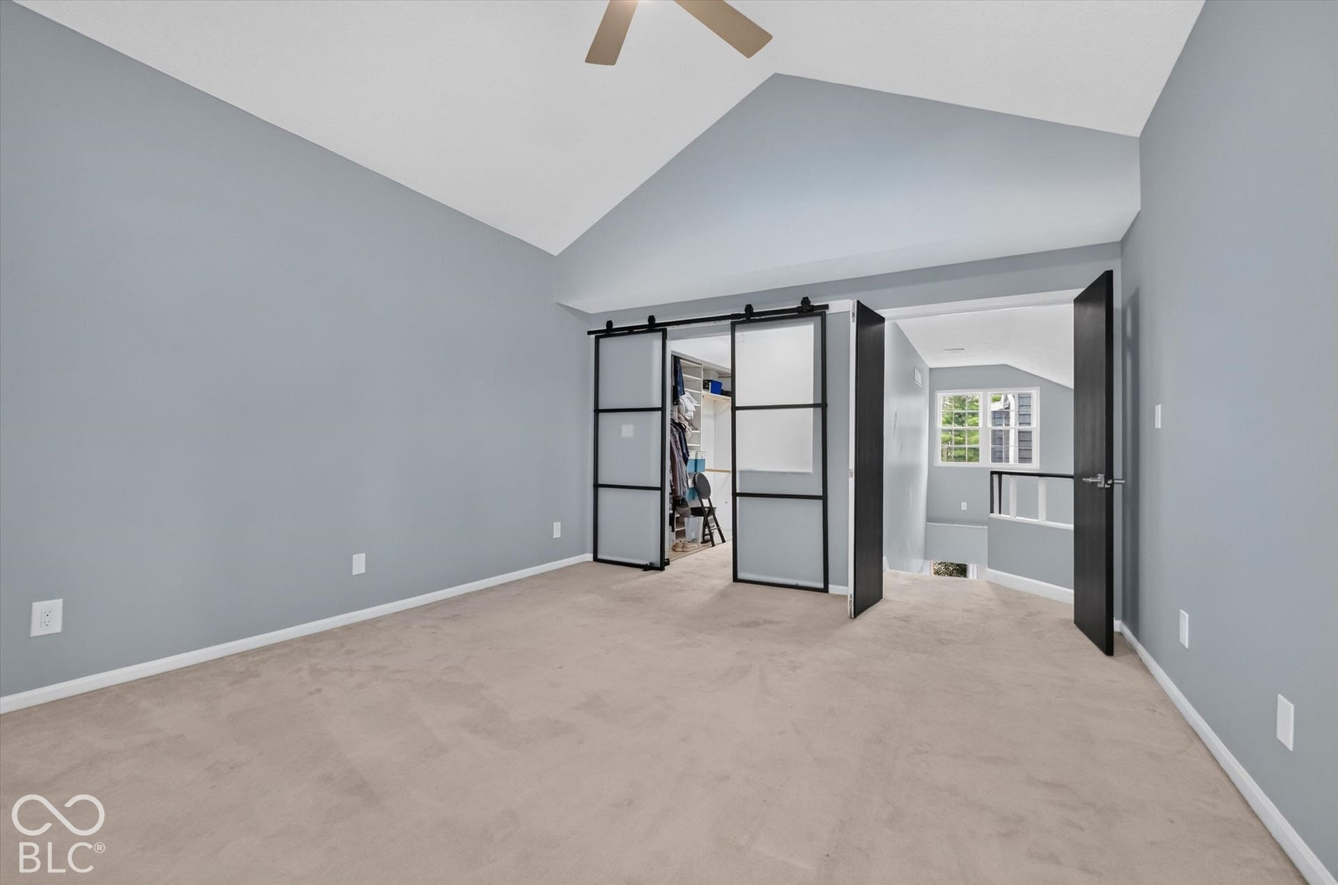 NEW CARPET INSTALLED after this photo was taken! Vaulted ceiling with ceiling fan, soft gray wall paint, light-toned carpet, black-framed sliding barn door, and a multi-pane window
