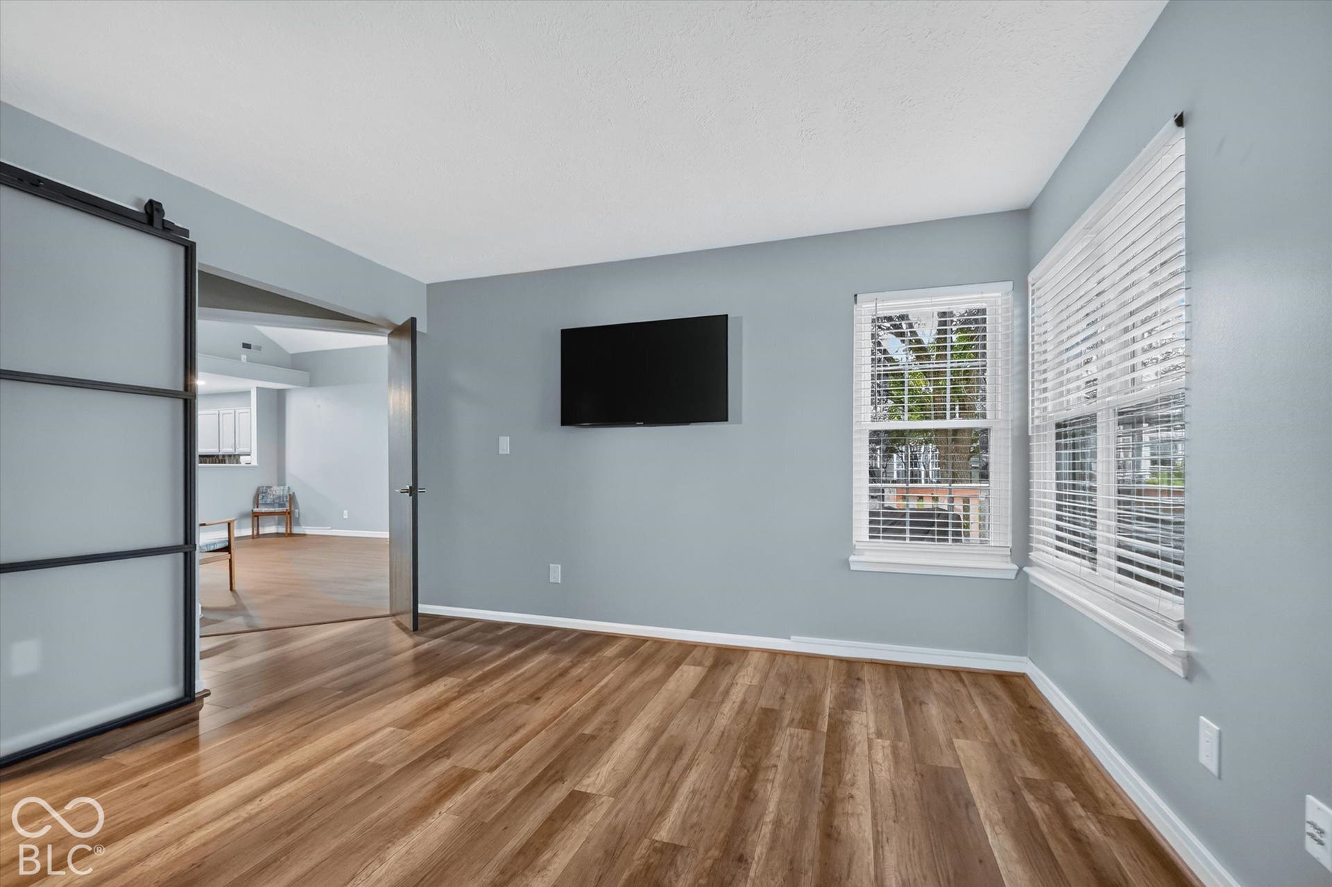 Wood-finish flooring throughout, light blue wall paint, multiple windows with blinds, and a barn-style sliding door