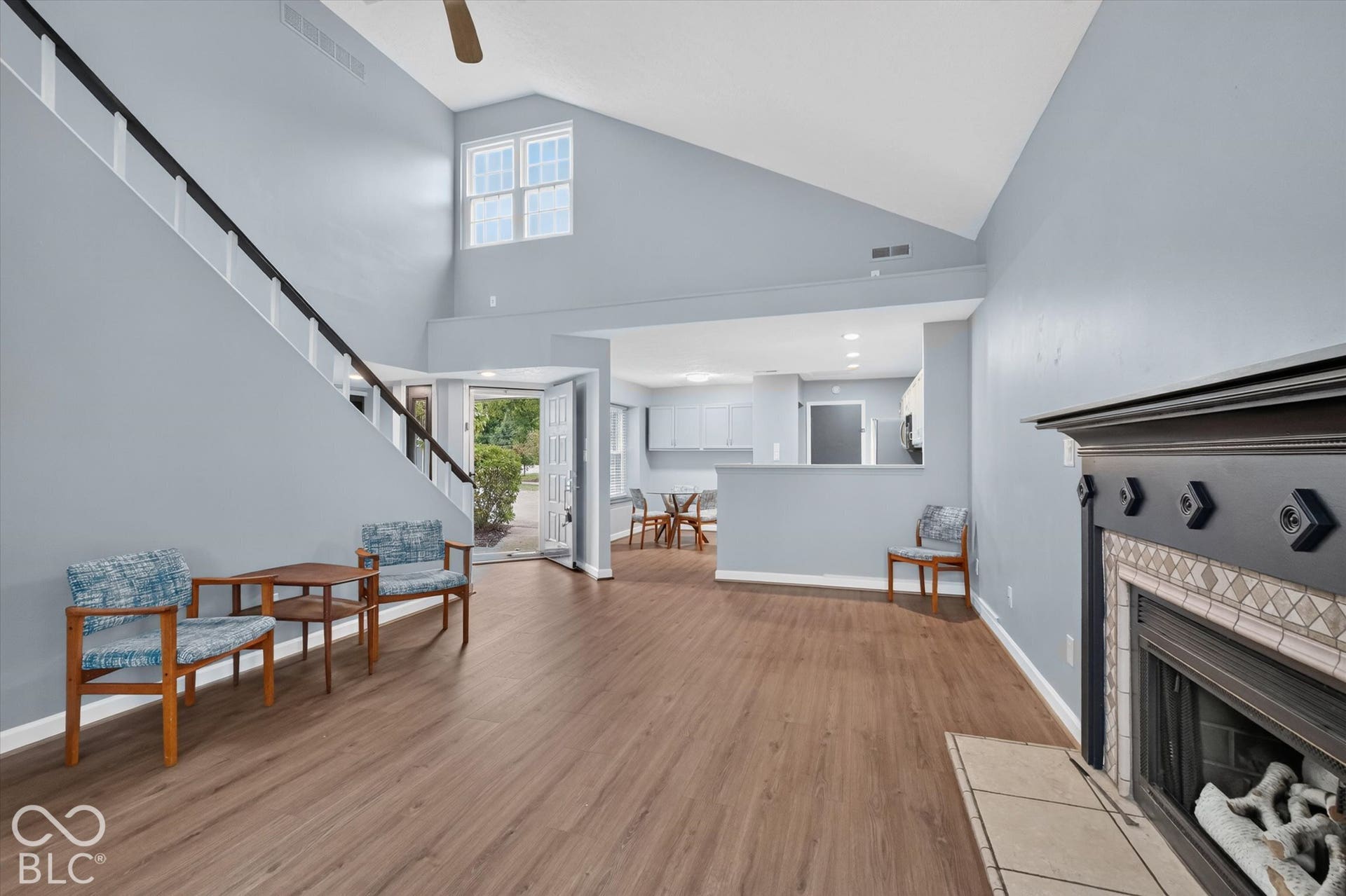 Vaulted ceiling, wood-finish flooring, staircase with black railing, fireplace with decorative tile surround, and upper-level windows
