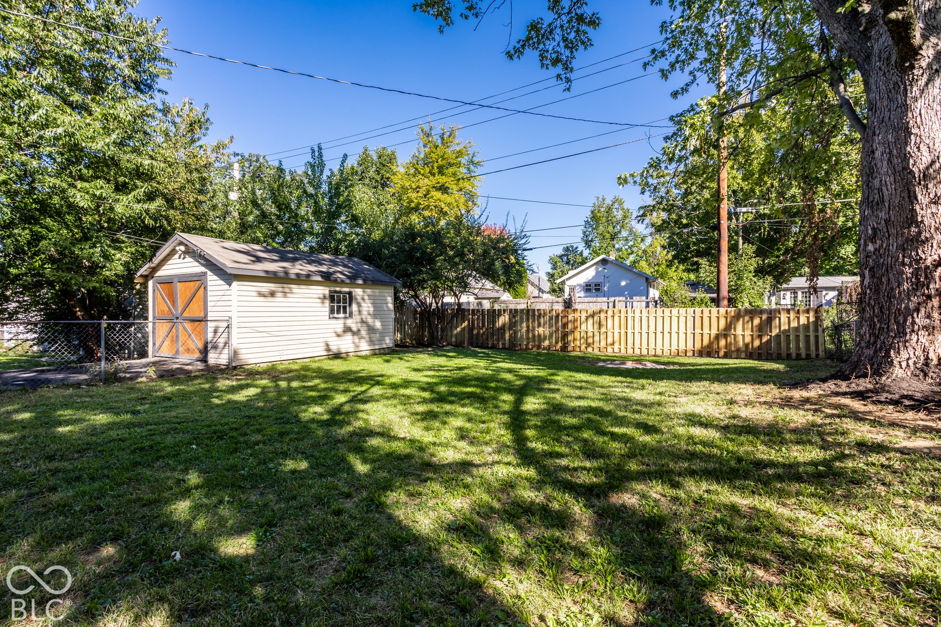 Expansive grassy area with a storage shed featuring wood doors, partial wood privacy fencing, and mature trees