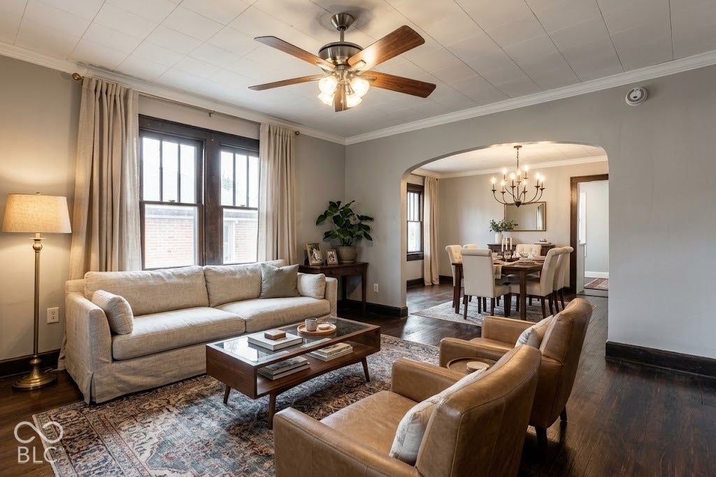 Virtually Altered - Dark wood-finish flooring, a ceiling fan with light fixture, and an arched entryway to an additional room featuring a chandelier