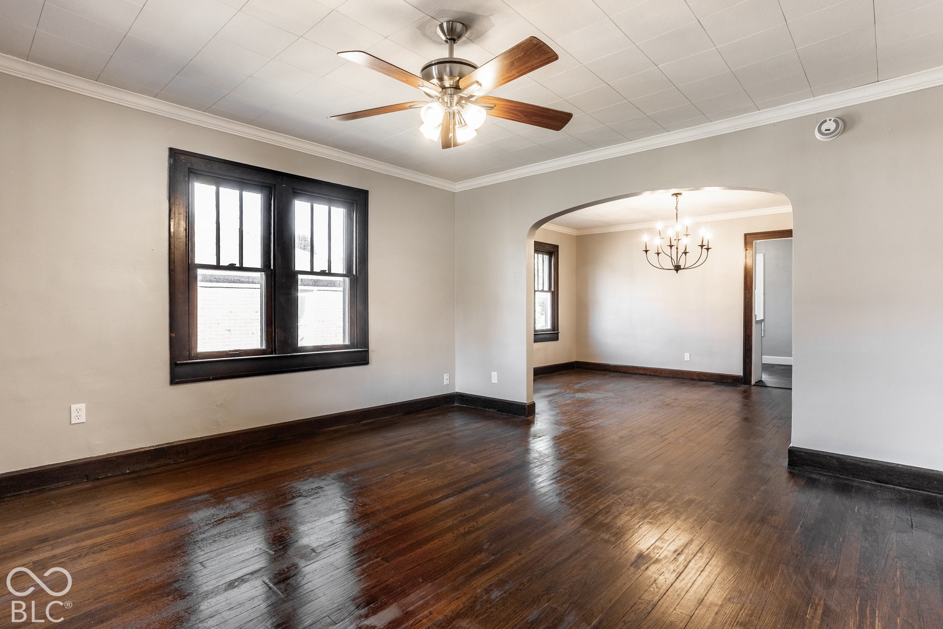 Hardwood flooring throughout, archway leading to additional space, dark wood trim, ceiling fan light fixture, and windows