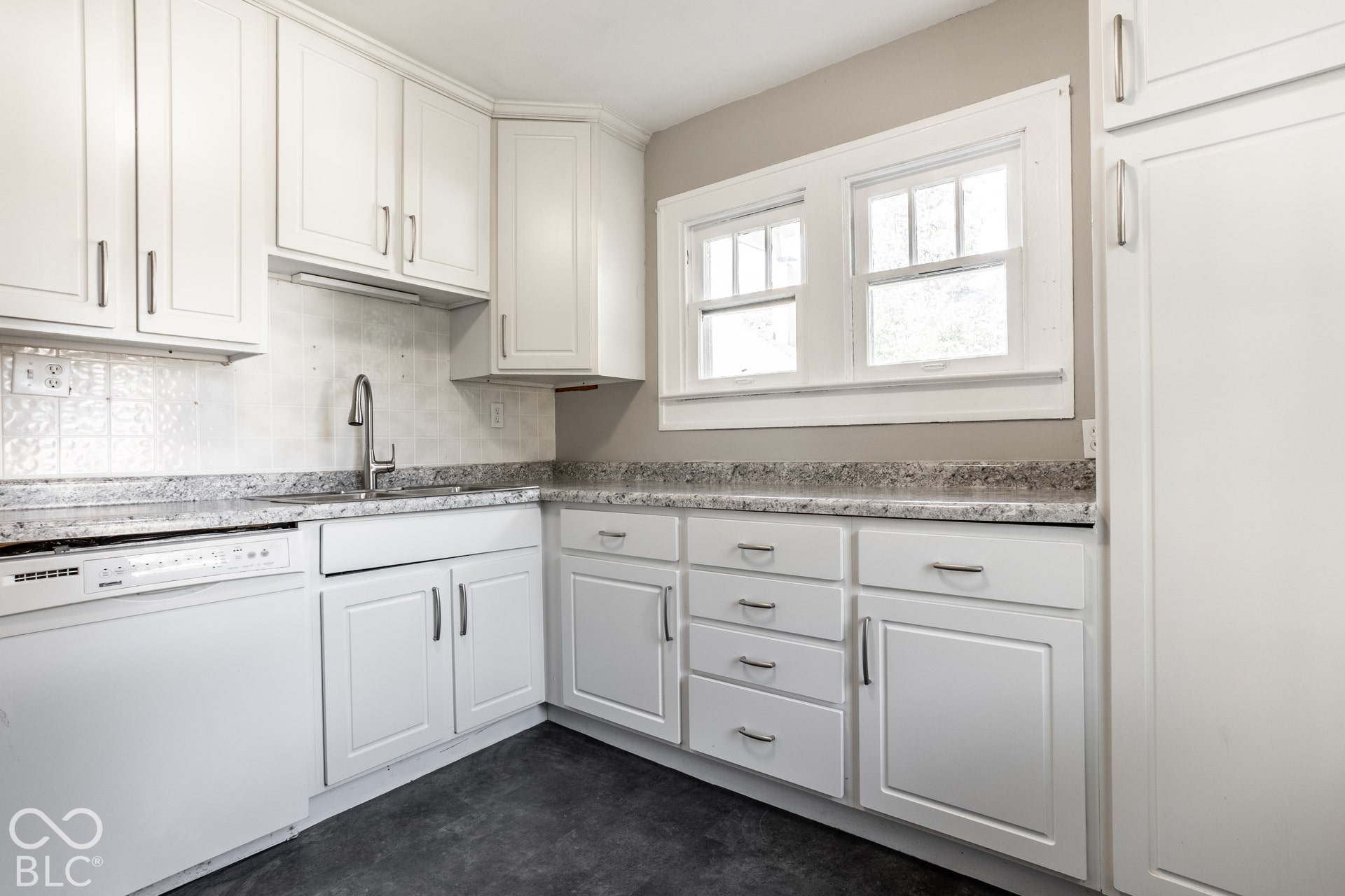 White shaker cabinetry with silver-tone hardware, textured tile backsplash, and a built-in dishwasher