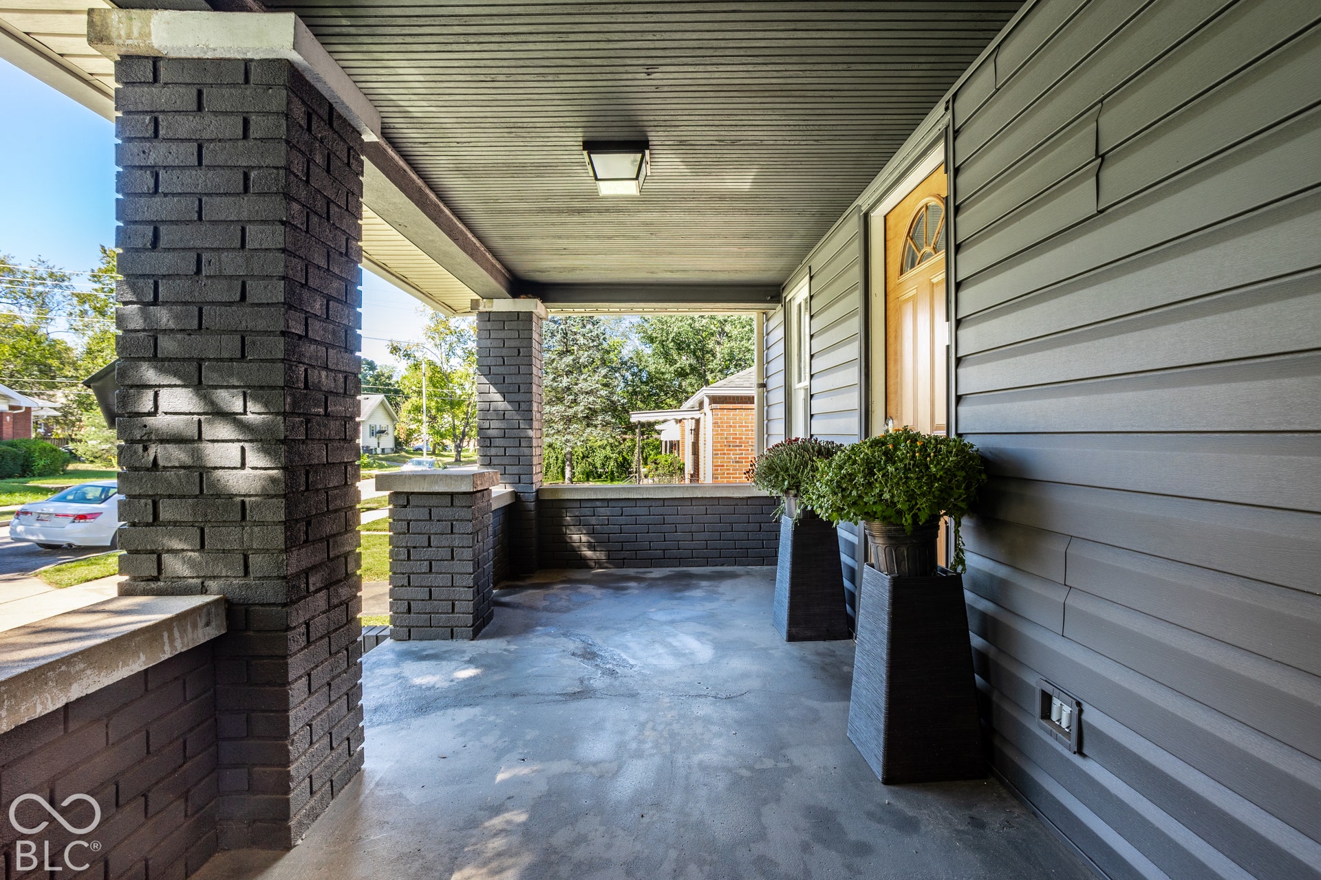 Covered front porch featuring dark brick columns, matching brick knee wall, and concrete flooring