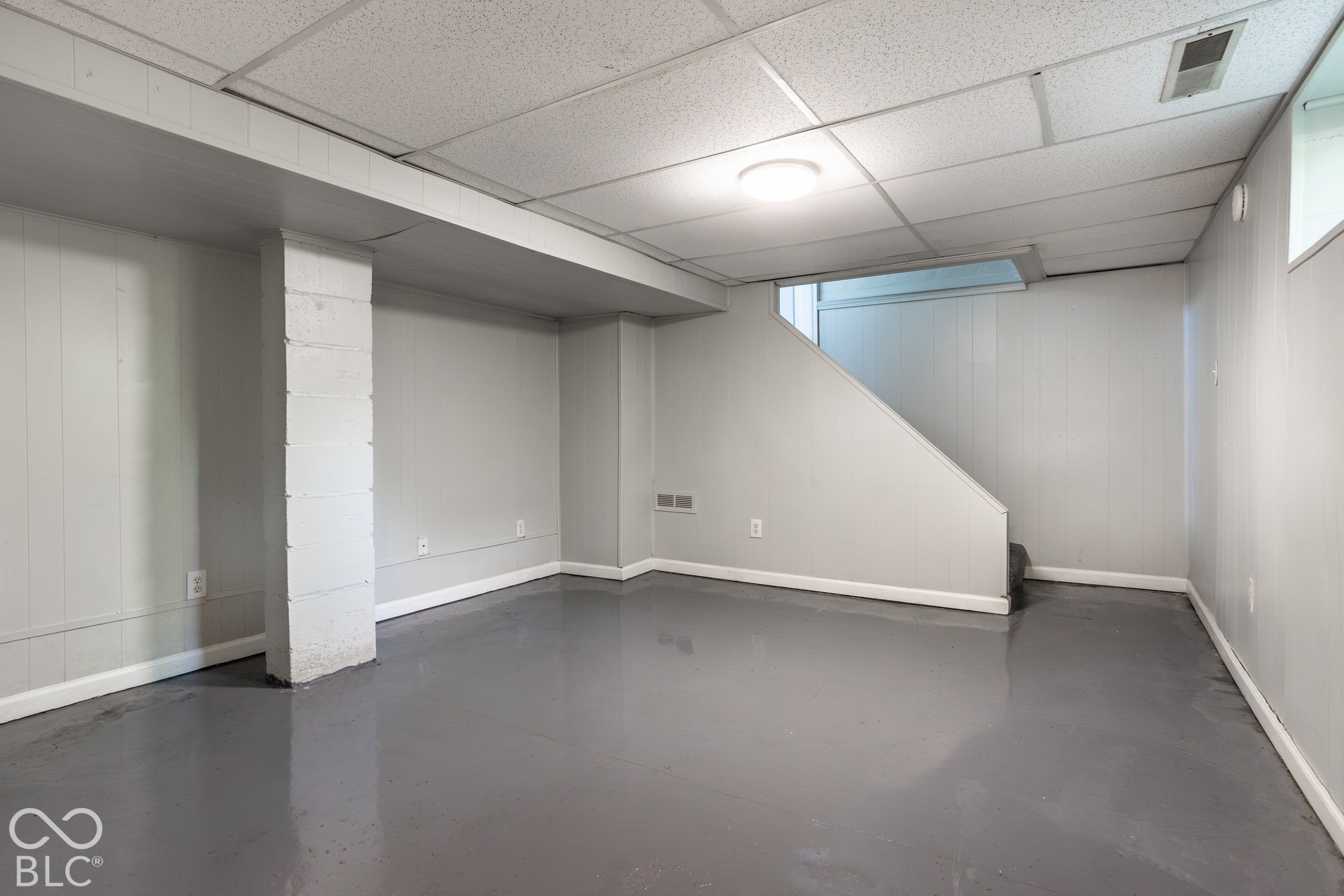 Basement living space - Spacious lower level featuring epoxy concrete flooring, light gray wall finishes, recessed lighting, drop ceiling, and an exposed structural column