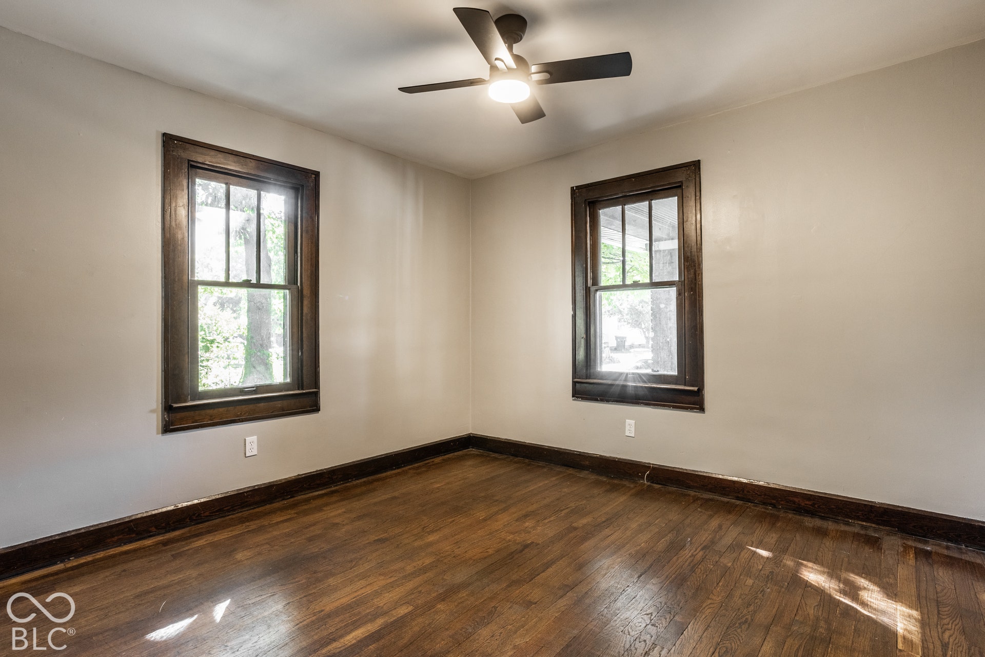 Bedroom 2 - Hardwood flooring, dark wood trim, two windows, and a ceiling fan with integrated lighting